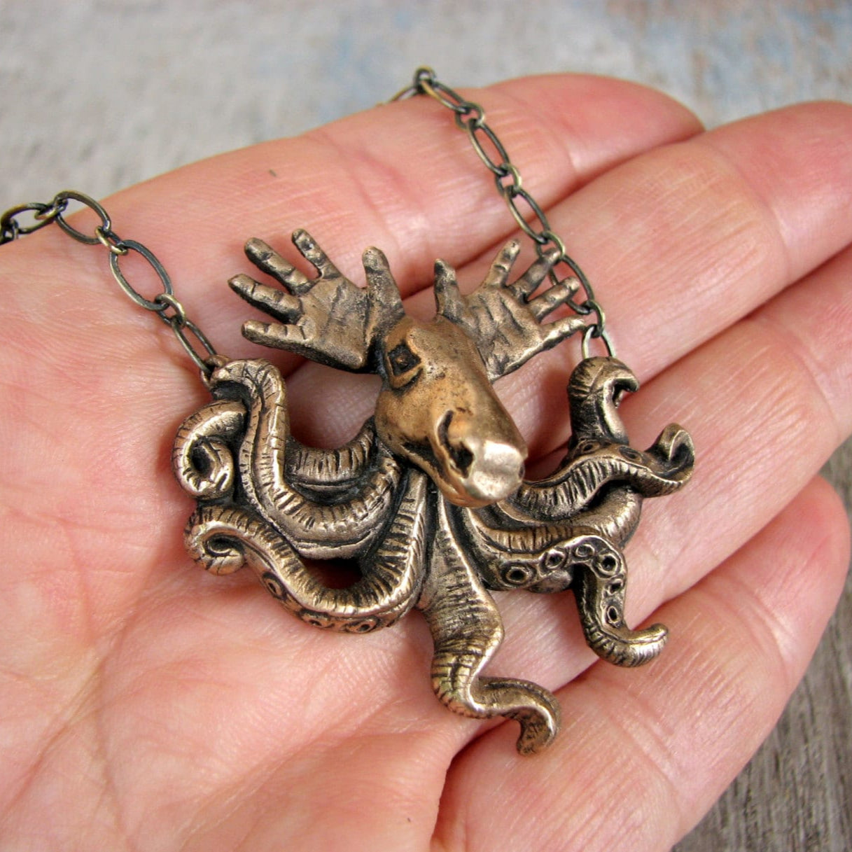 A bronze pendant featuring a surreal creature with tentacles and antlers, resembling a moose with hands as antlers