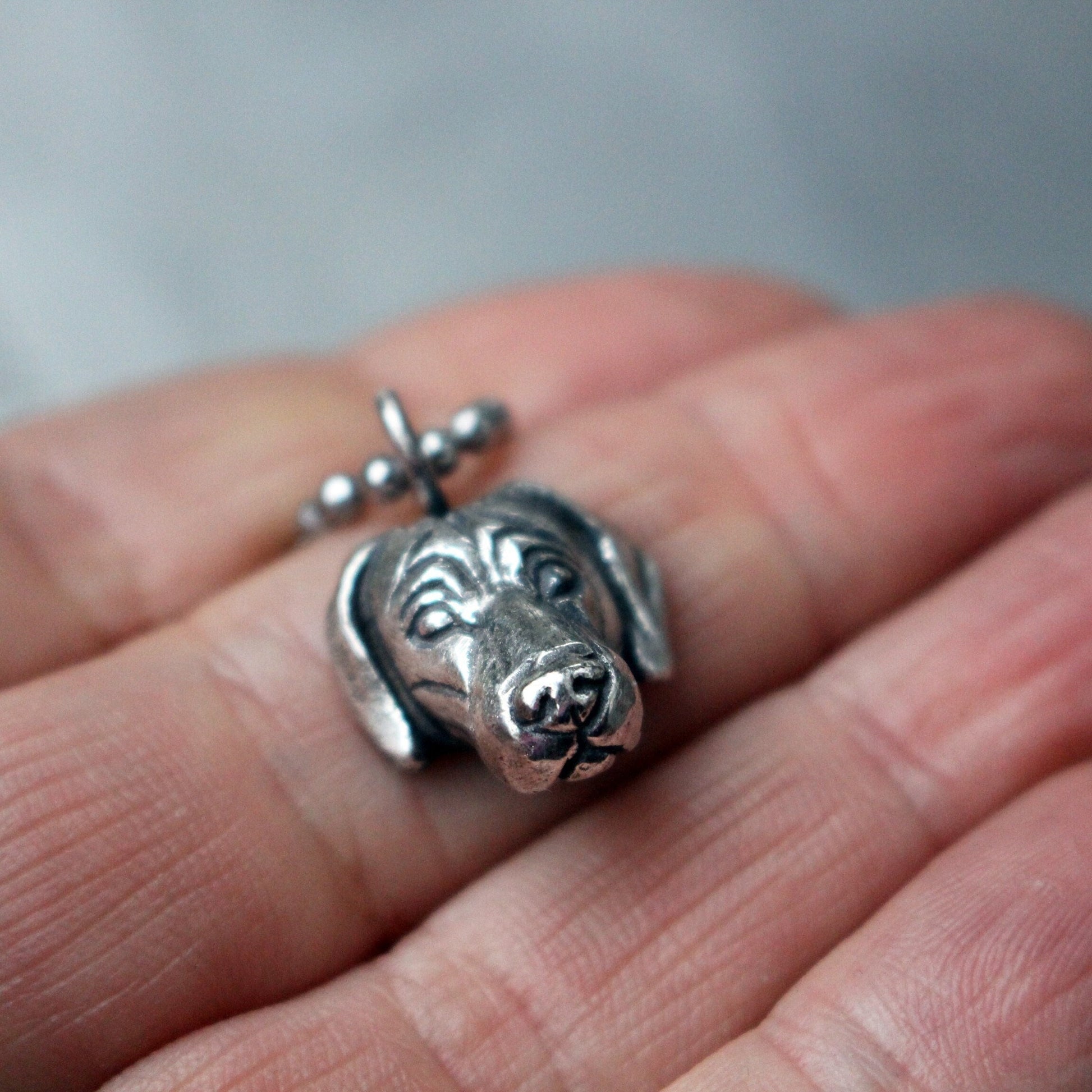 A sterling silver pendant in the shape of a Weimaraner dog head, held between fingers.