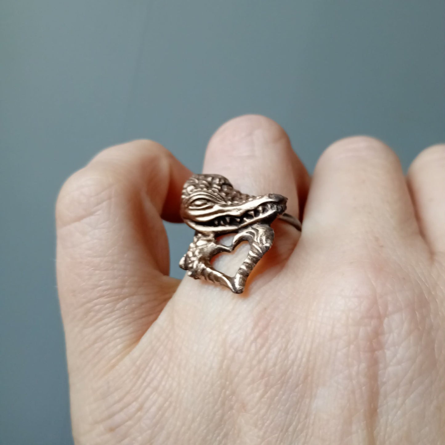 Bronze ring with a alligator design on a finger against a gray background