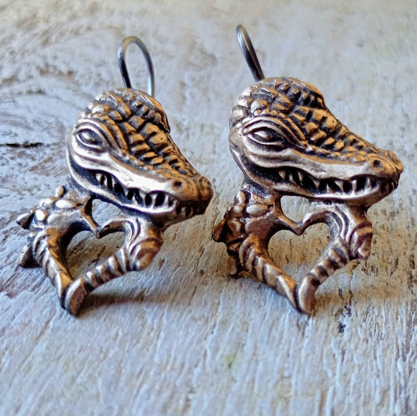 Pair of bronze alligator head earrings on a textured surface
