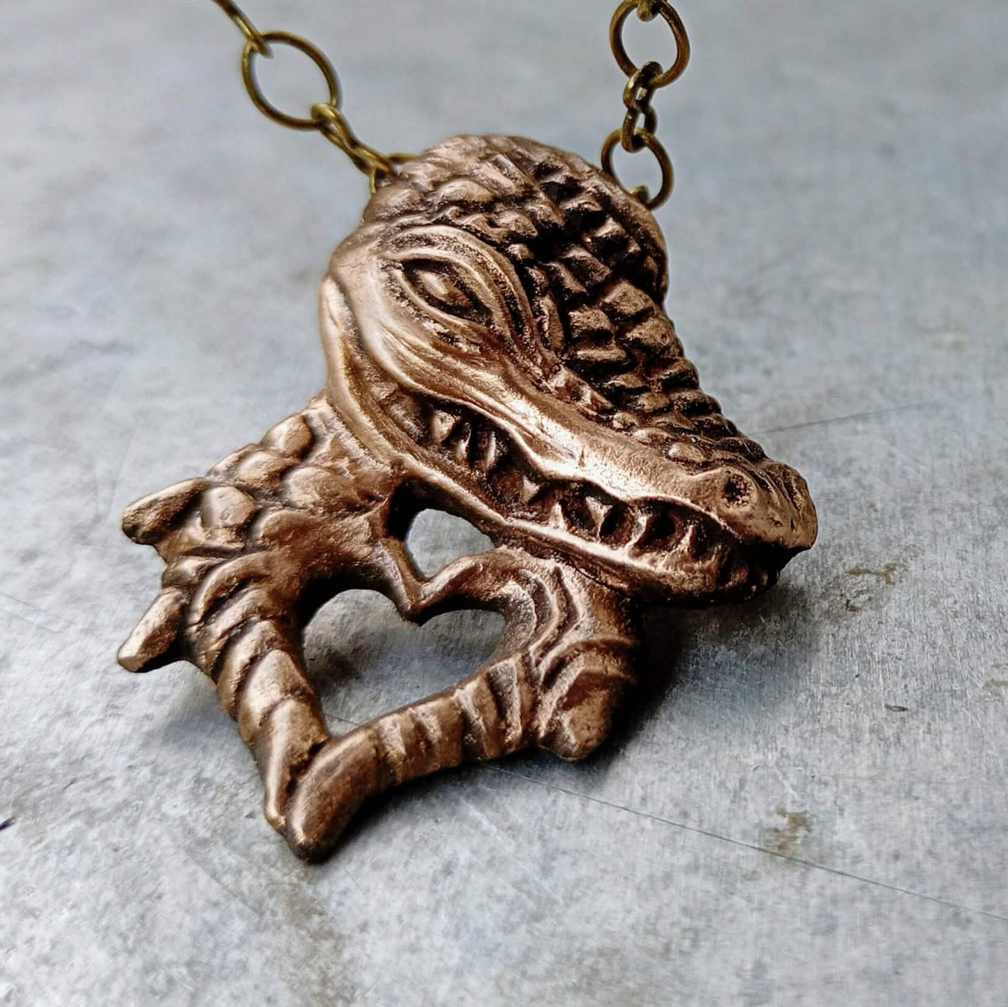 halsband med en krokodil skulpterad i brons, krokodilen formar ett hjärta med sina händet/klor