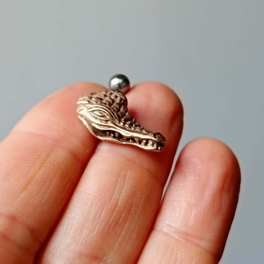 Bronze alligator belly ring piercing on a finger with a gray background