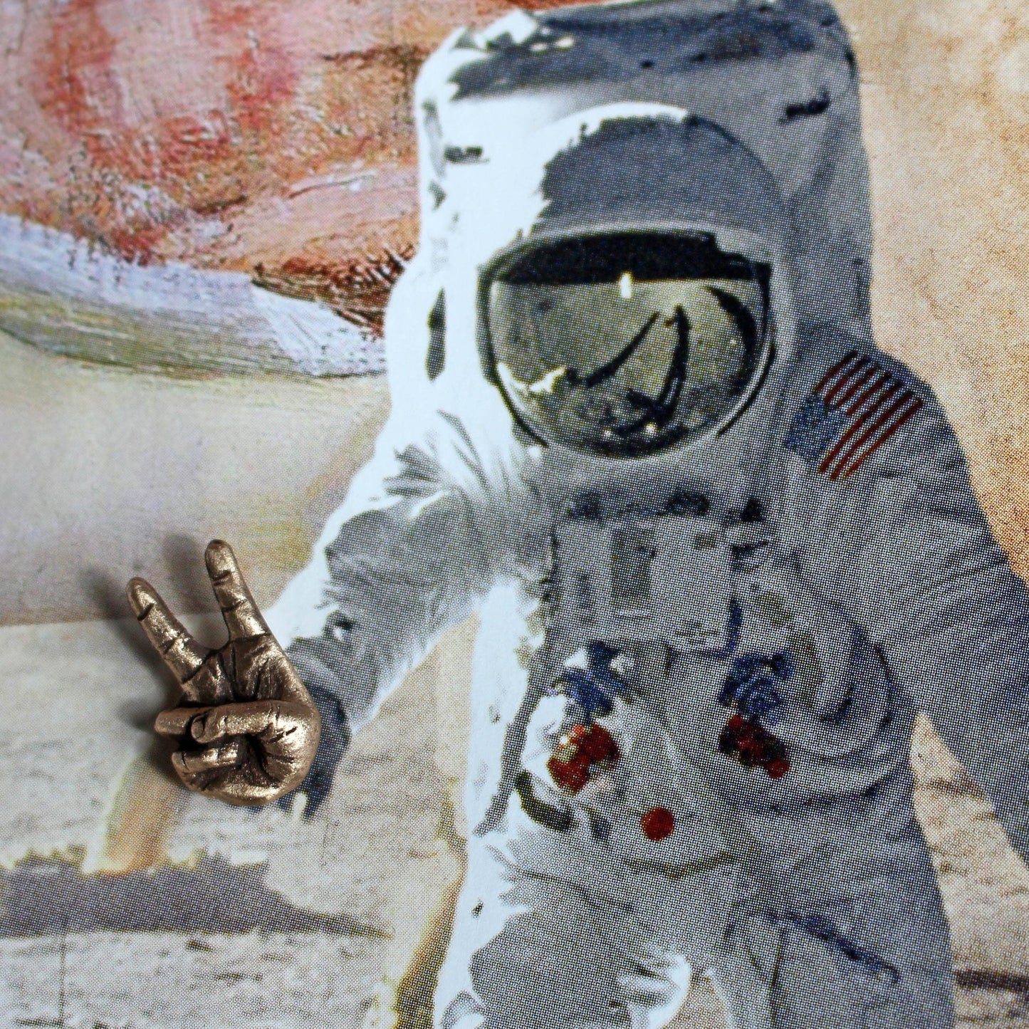 a sculpted bronze hand making the victory sign, displayed on a picture of an astronaut, which makes it look like the astronaut is making the hand sign