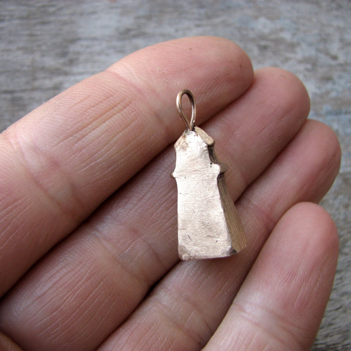 baksida, Halsbands hänge med en liten fyr skulpterad i brons