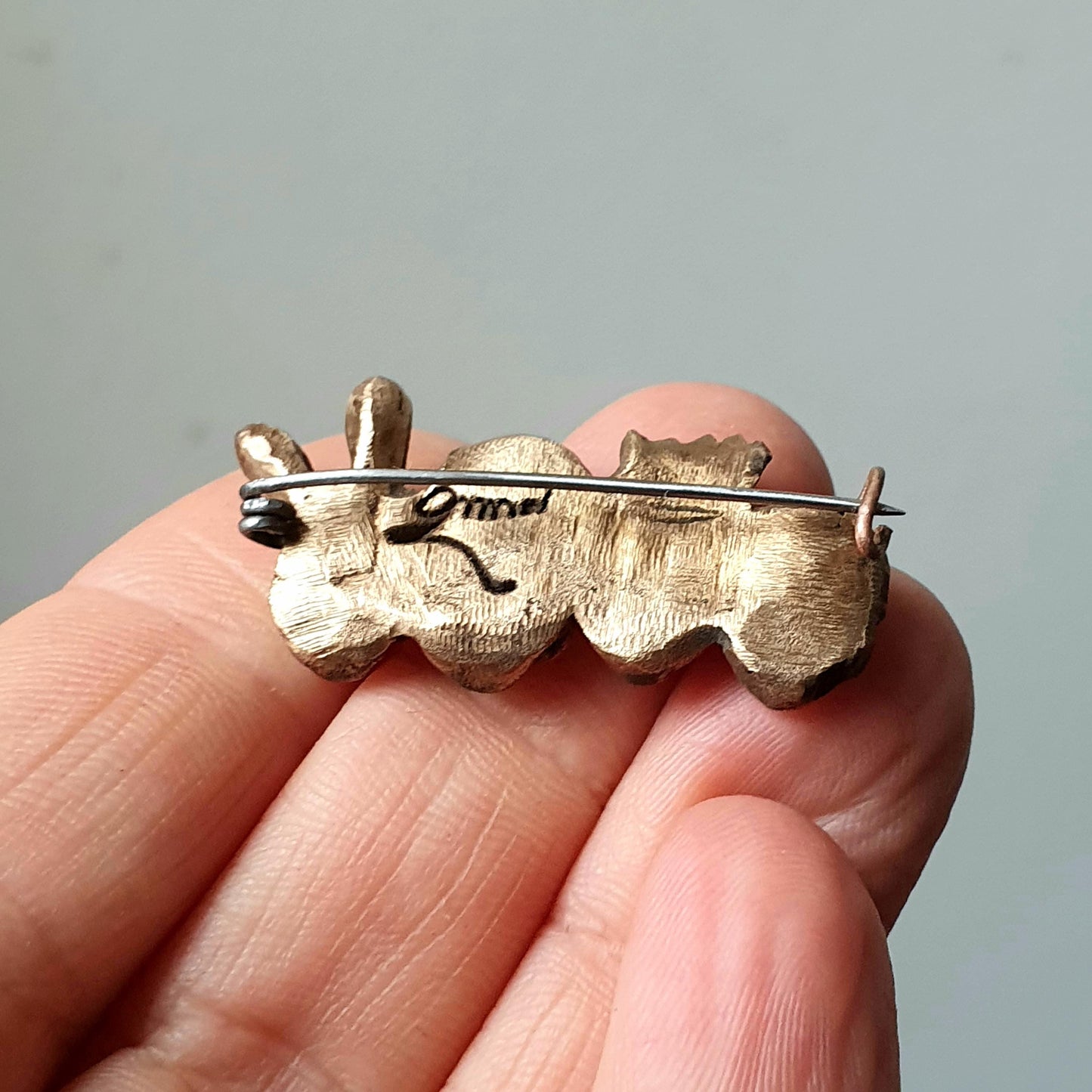 backside, brooch featuring a four skulls wearing partyhats, such as a crown and bunny ears, on a metallic surface.