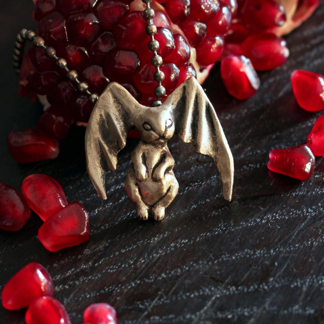 Bronze bat- bunny pendant on a dark surface with red pomegranate seeds