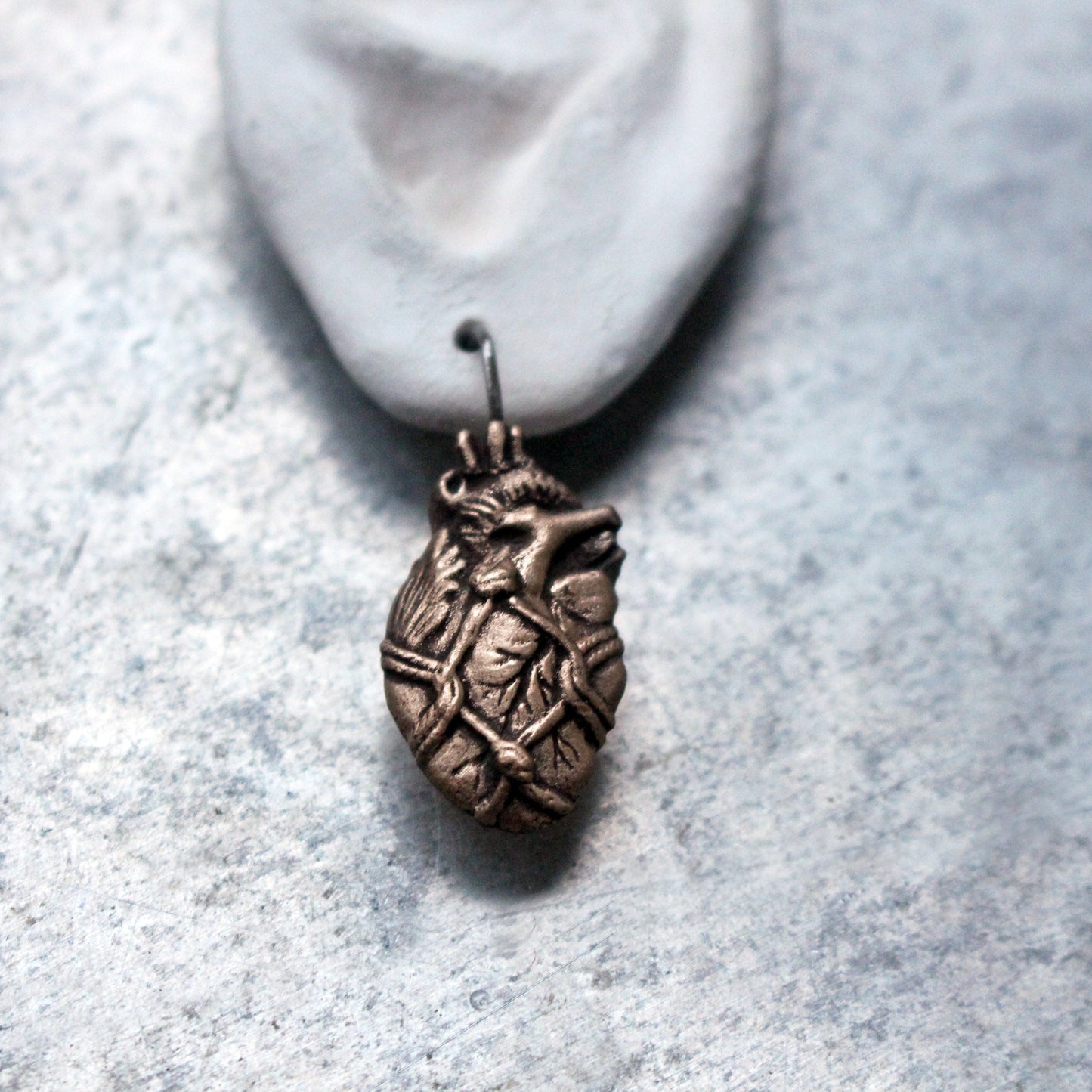 Handmade bronze anatomical heart earrings bound with rope, displayed on a mannequin ear.