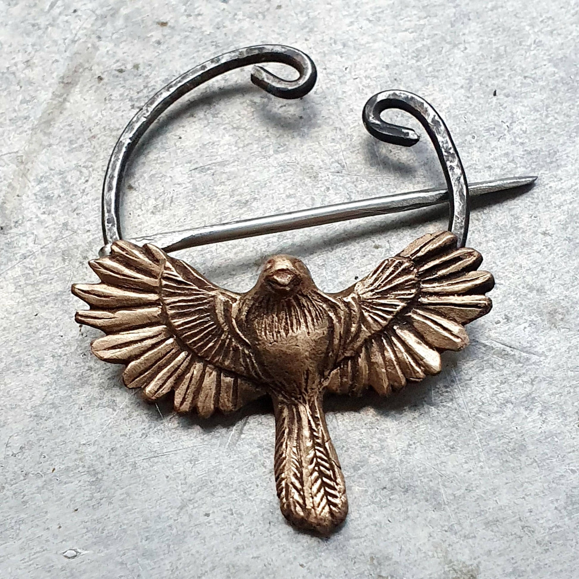 A bronze-colored bird in flight brooch with a stainless steel circle and pin.