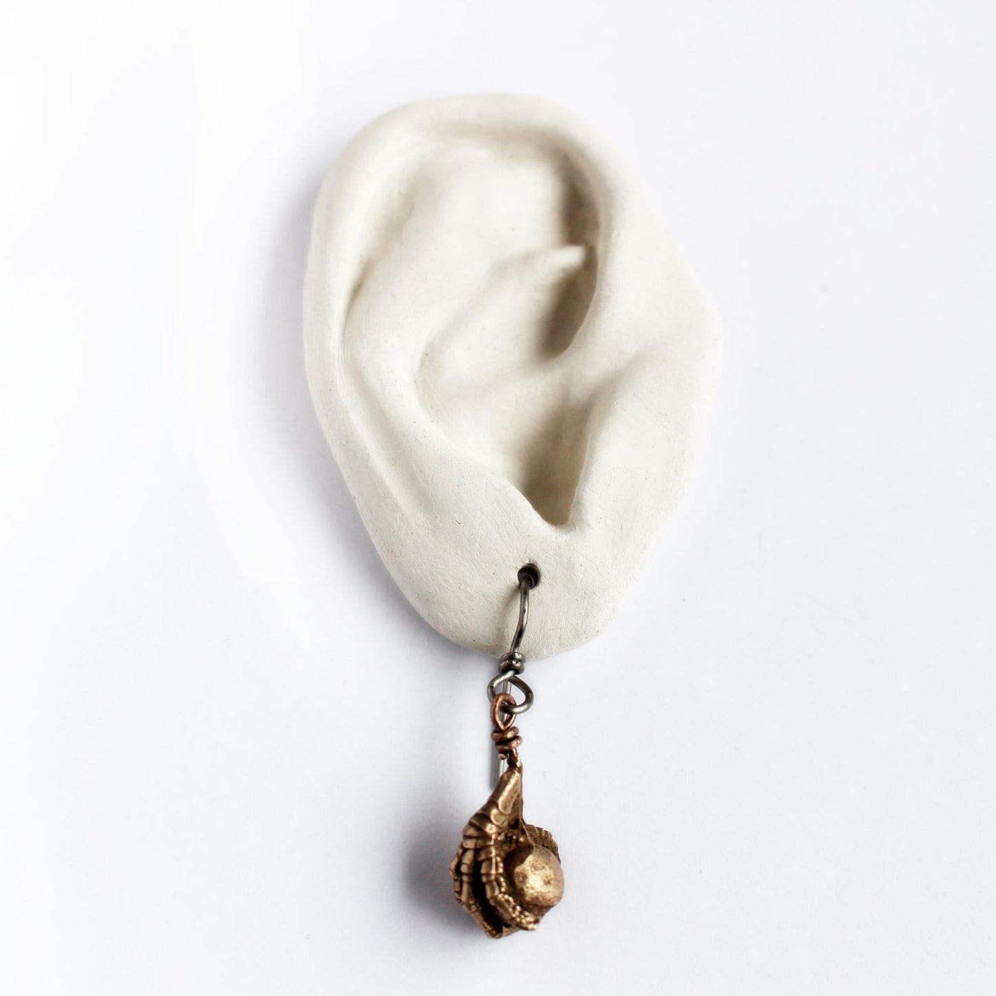 Earring with a bird claw grasping a bead on a white ear model with a white background