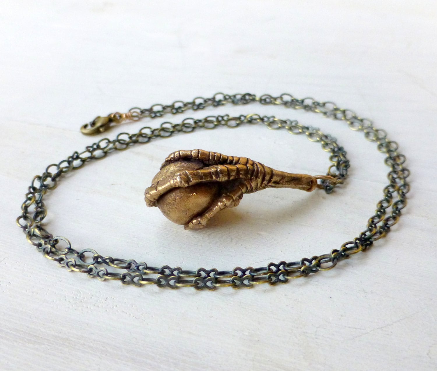 Bronze pendant depicting a bird claw grasping a bead, attached to a chain.