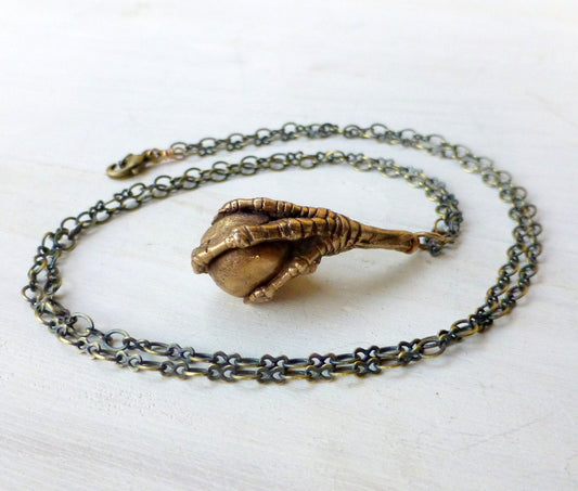Bronze pendant depicting a bird claw grasping a bead, attached to a chain.
