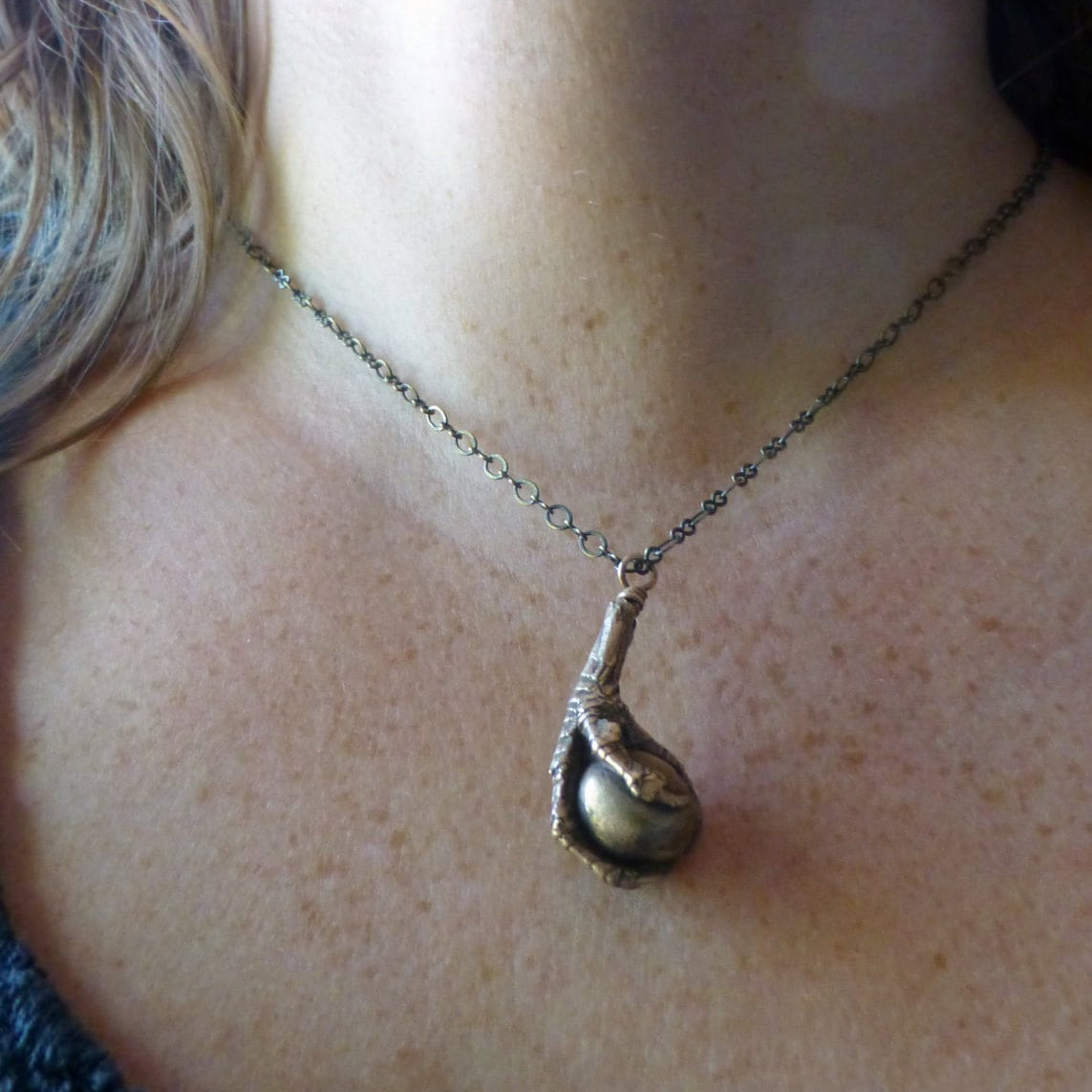handgjort brons halsband med en fågelklo som håller i ett klot på halsen av modell