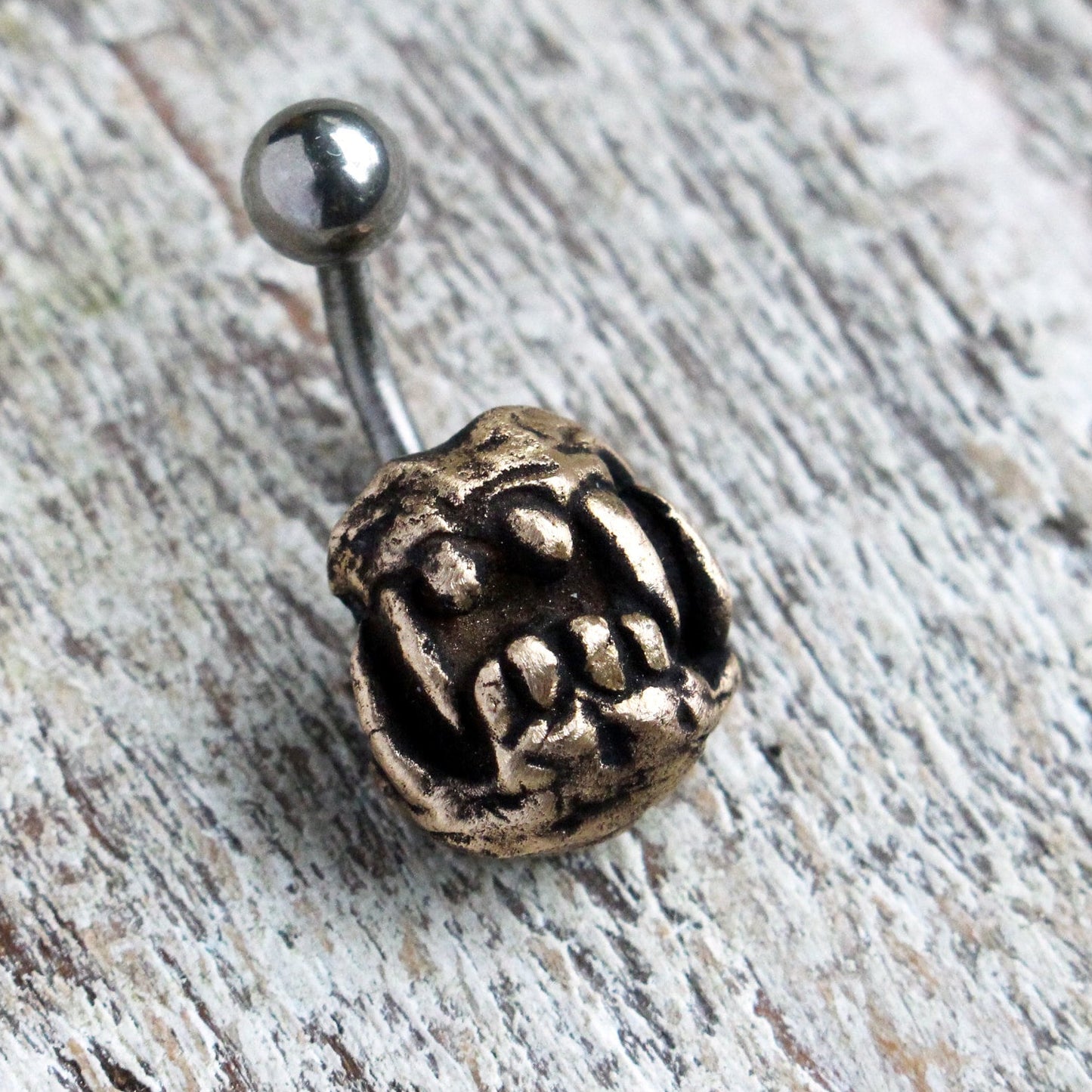 A belly button ring with a sculpted monster/dragon skull design, attached to a barbell made of either titanium or surgical steel.