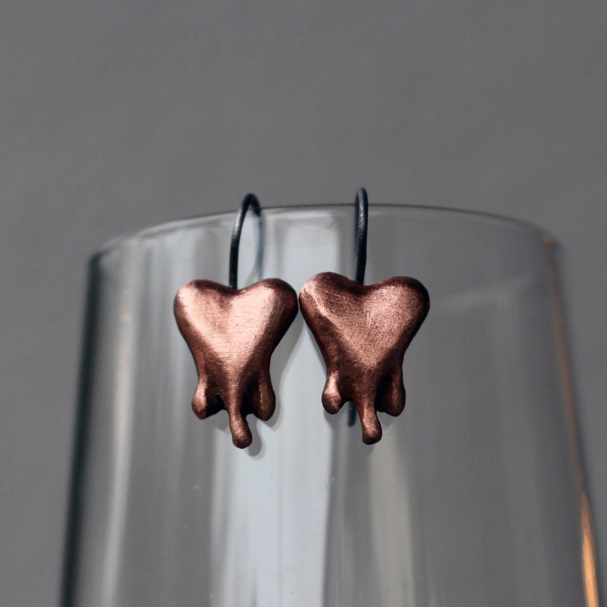 A pair of copper heart-shaped earrings finish, the hearts look like they are bleading, melting or dripping