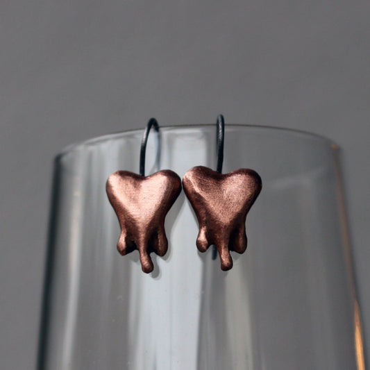 A pair of copper heart-shaped earrings finish, the hearts look like they are bleading, melting or dripping