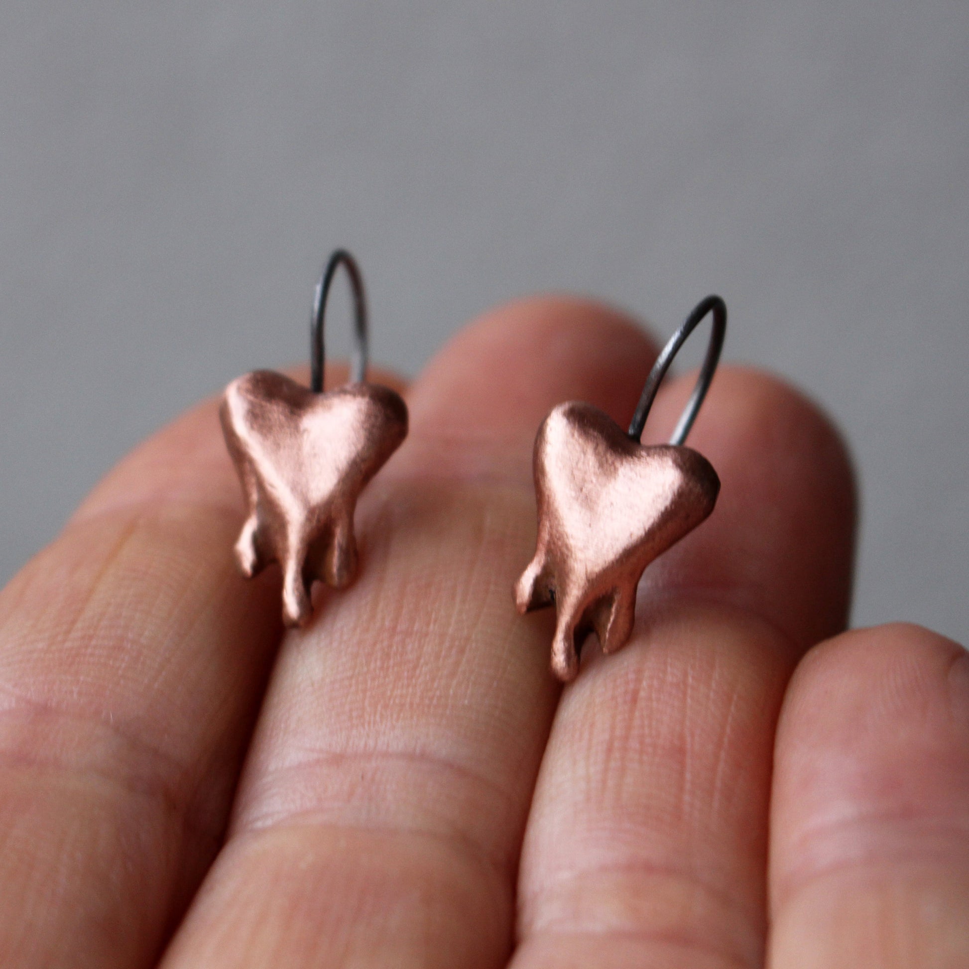 A pair of copper heart-shaped earrings finish, the hearts look like they are bleading, melting or dripping