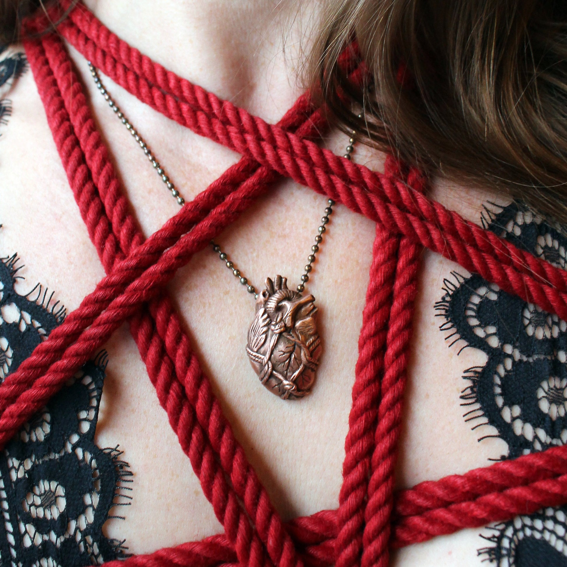 A realistic heart-shaped pendant necklace made from copper clay, bound with red rope, displayed on a person's chest.