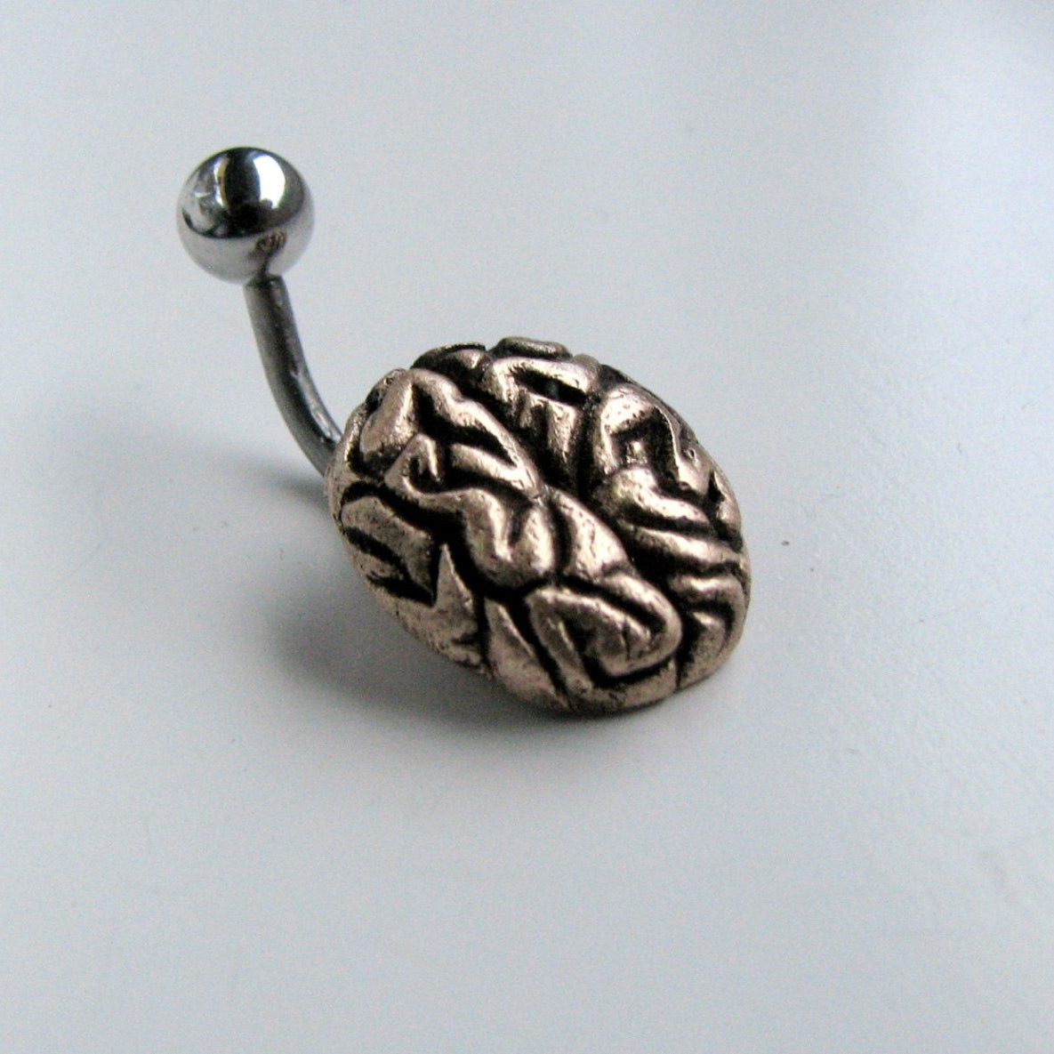 A belly button ring with a bronze sculptured brain design attached to a curved barbell with a steel ball on one end.