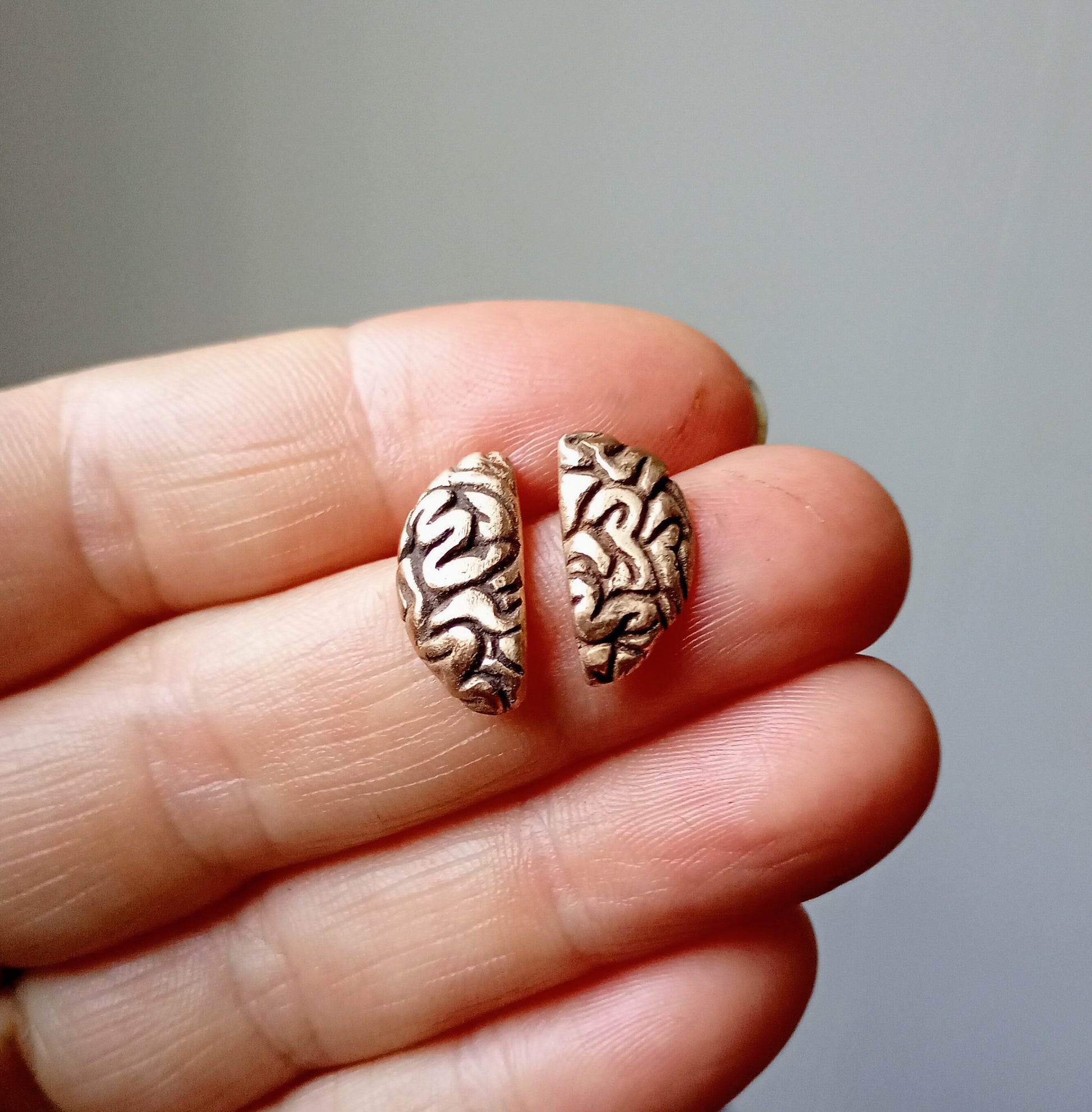Bronze brain-shaped earrings held between fingers against a neutral background