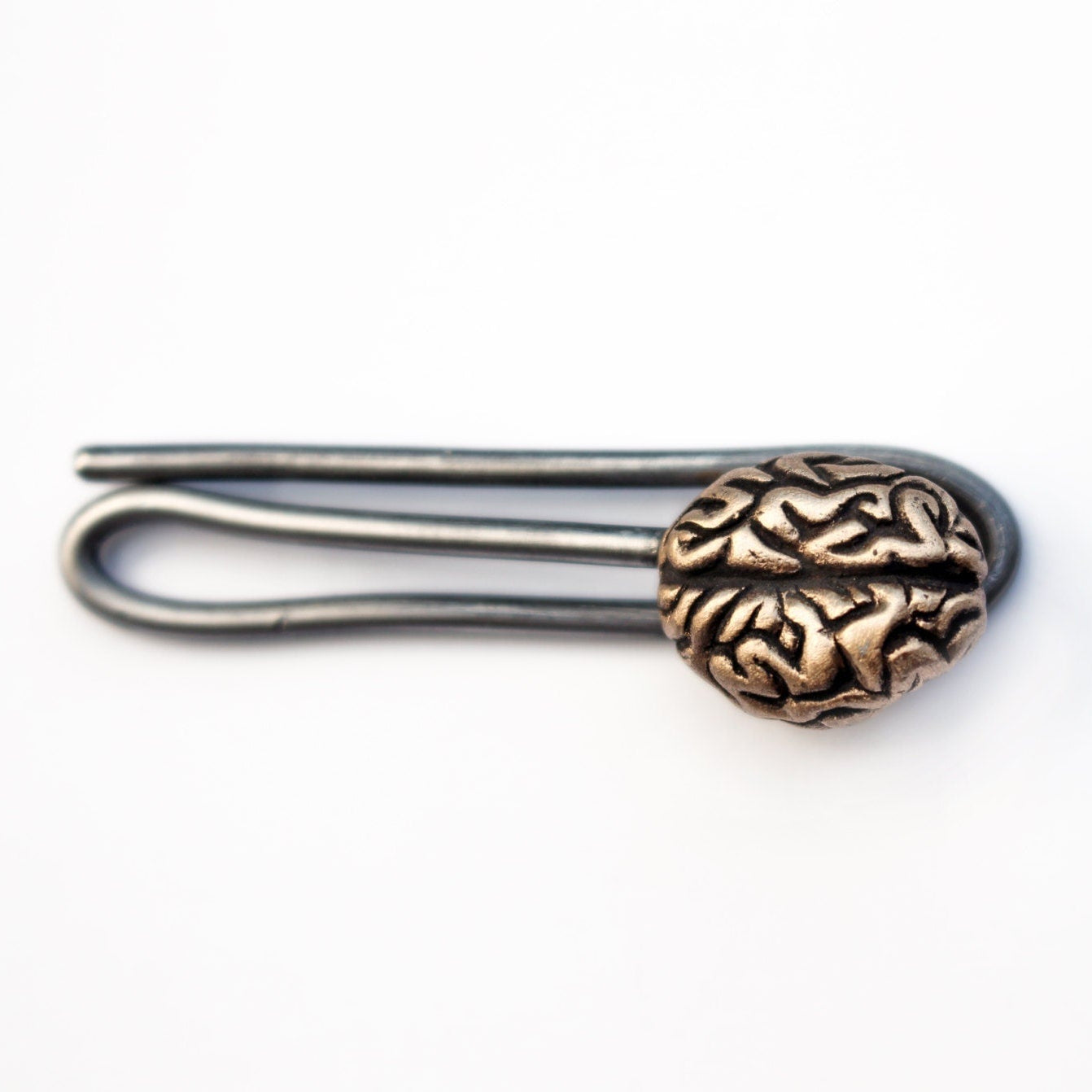 A bronze brain tie bar with a simplified human anatomy design, attached to a stainless steel wire clip.