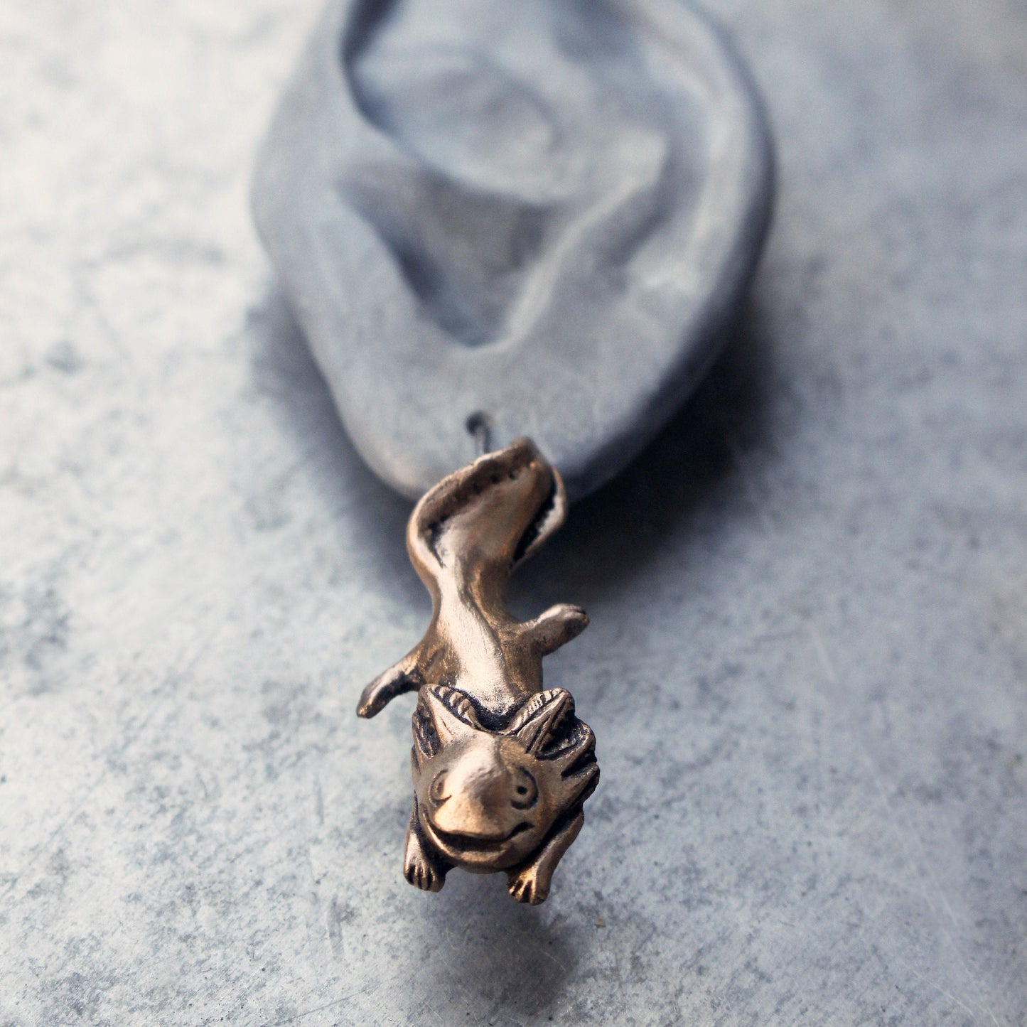 handmade axolotl earrings made from bronze hanging from a ceramic ear