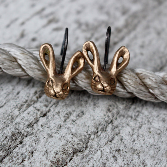 A pair of bronze bunny rabbit earrings with titanium ear wires, displayed against a textured background.