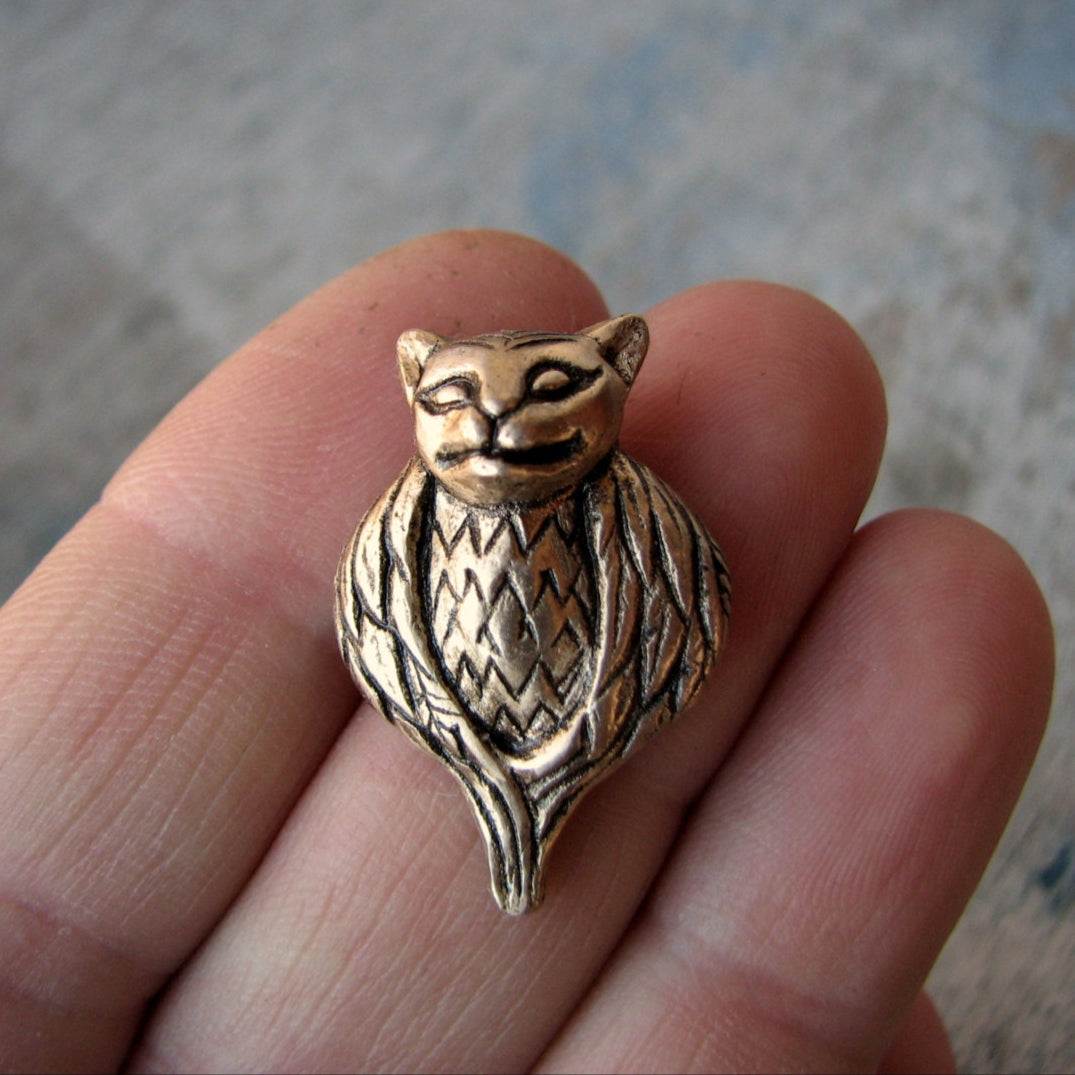 Bronze cat and bird mixed creature  pendant held between fingers on a neutral background