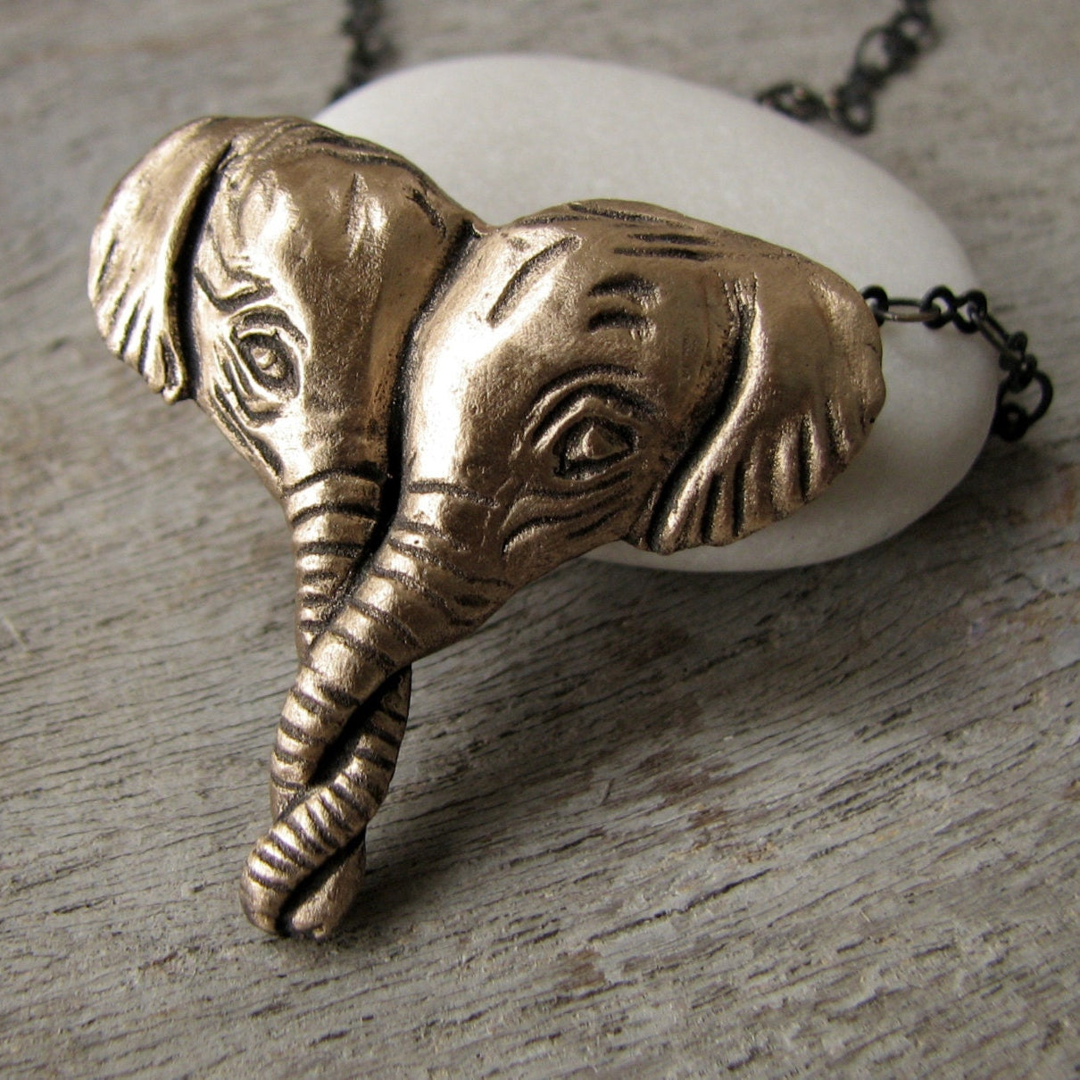 A necklace with a pendant featuring two elephant heads in a heart shape, crafted from metal with bronze