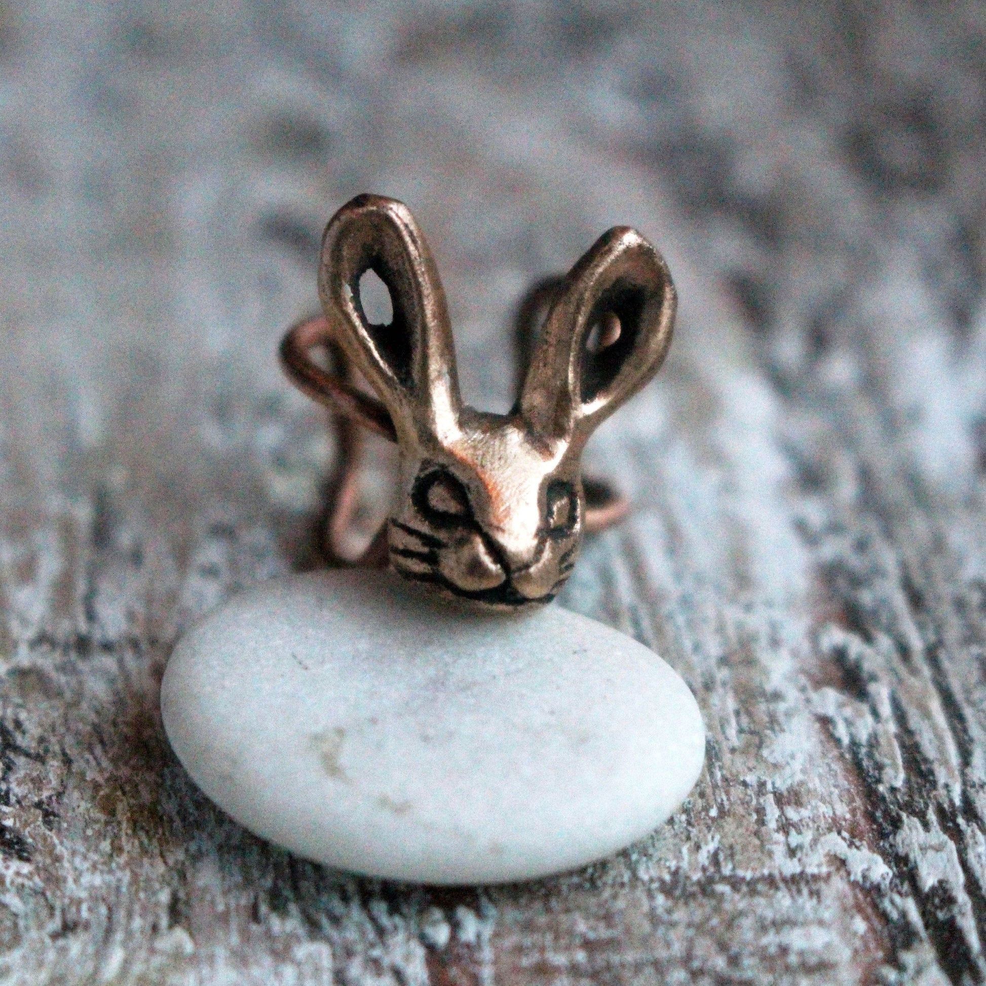 A bronze bunny rabbit ear cuff displayed on a white stone, set against a wooden background.