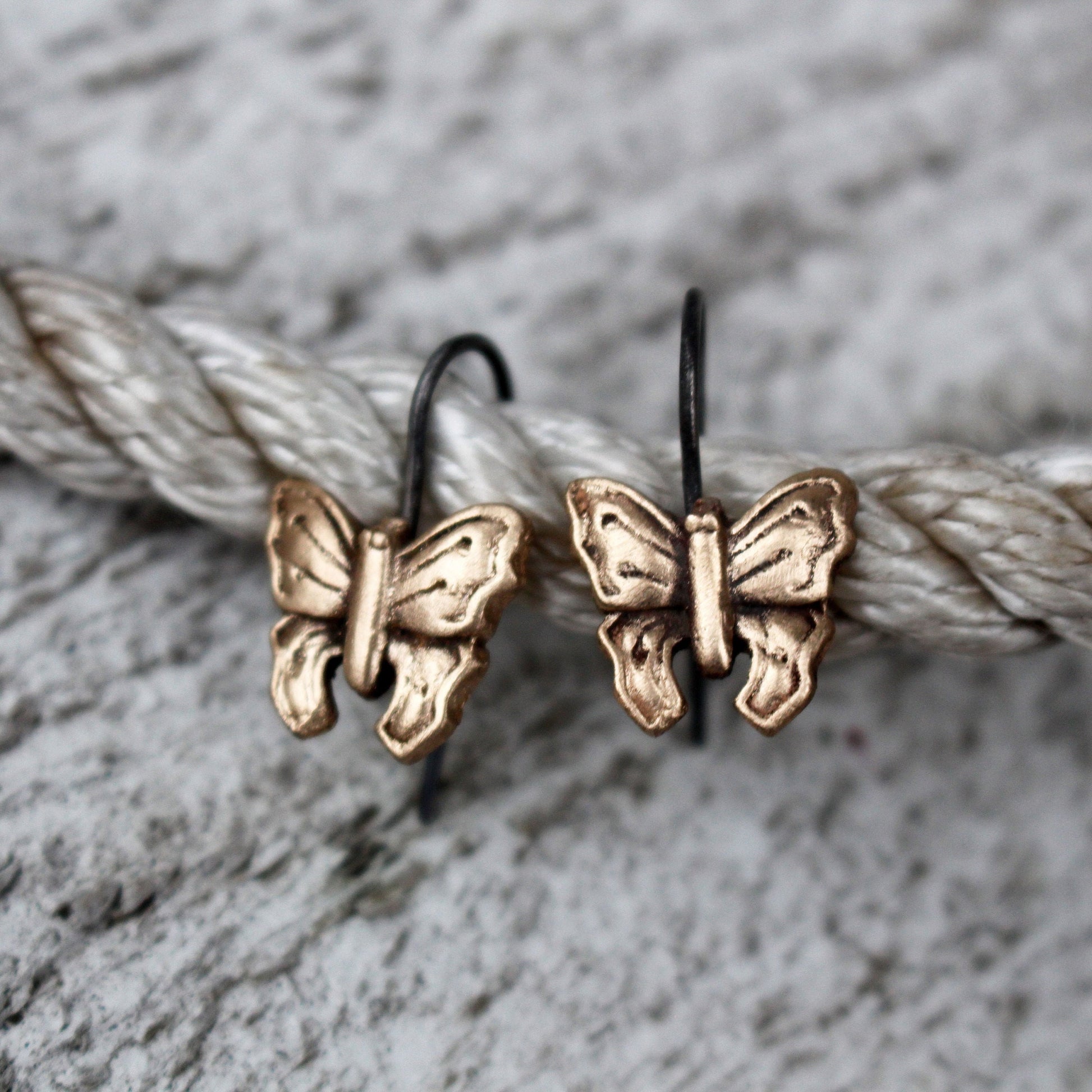 A pair of bronze and titanium butterfly earrings dangle from titanium hooks, resting on a textured white surface.