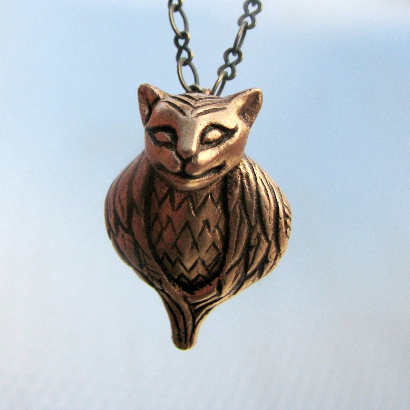 Bronze cat with bird body pendant on a chain against a light blue background