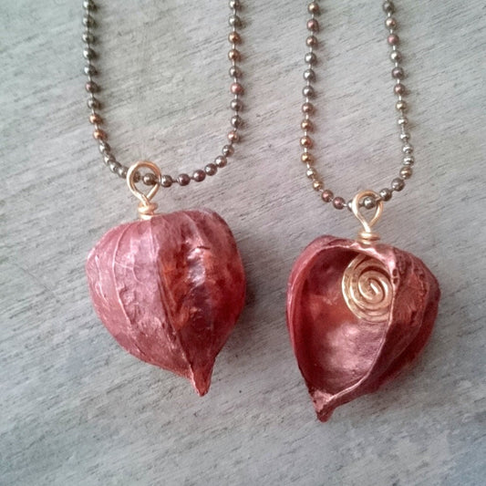 Two copper pendants in the shape of Chinese lanterns or winter cherries, with one showing the front and the other showing the side, both with a ball chain necklace.
