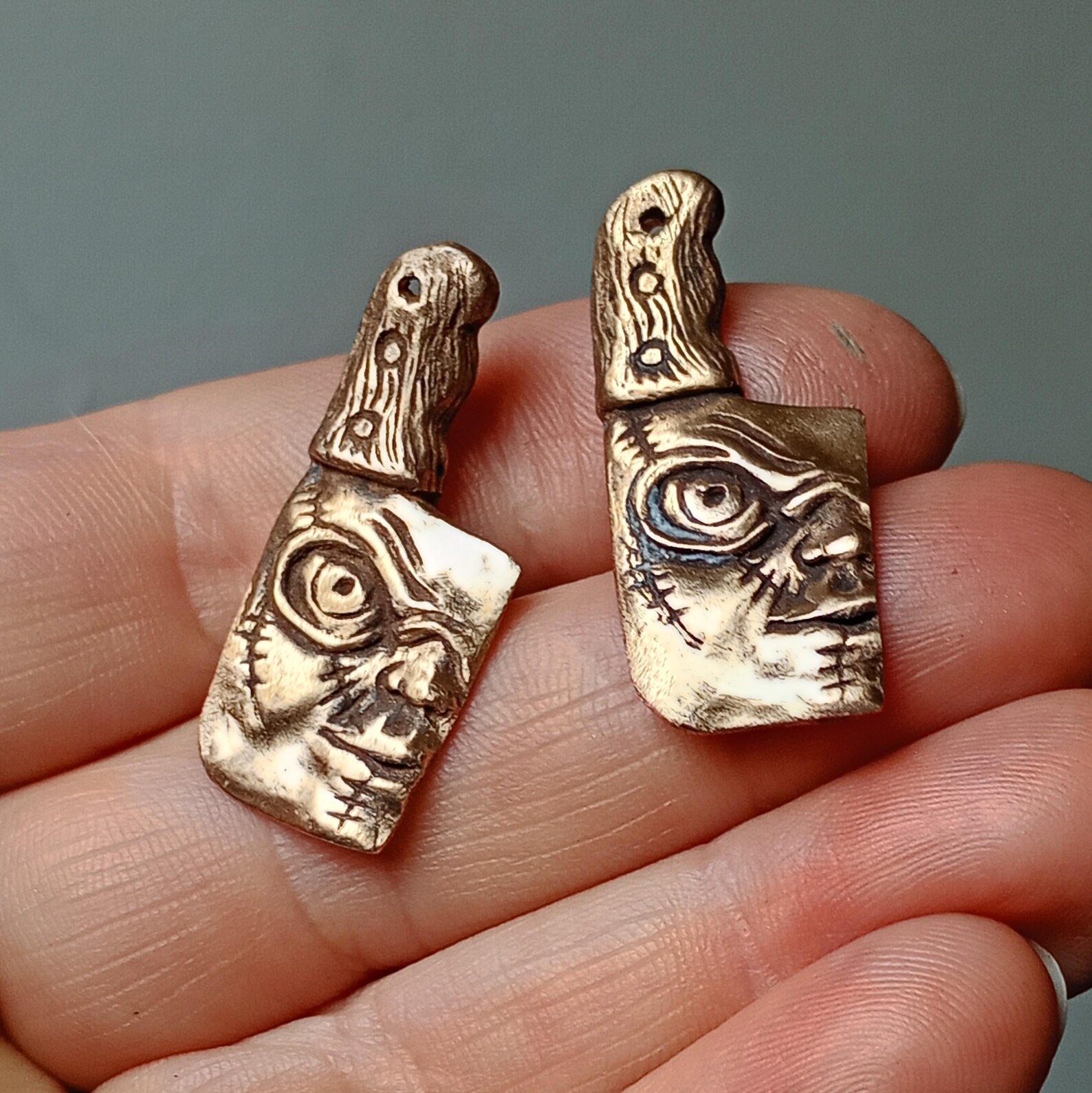 Bronze knife-shaped cuff links with Chuckys face designs held between fingers against a neutral background