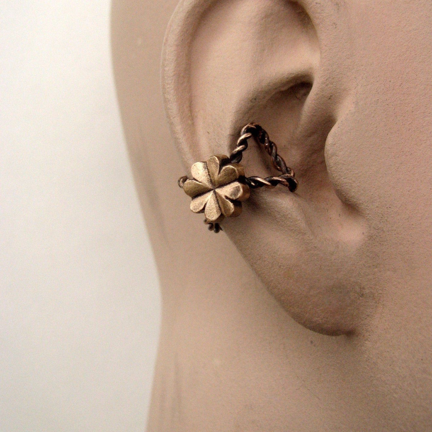 A bronze ear cuff featuring a clover design, displayed on an ear mannequin.