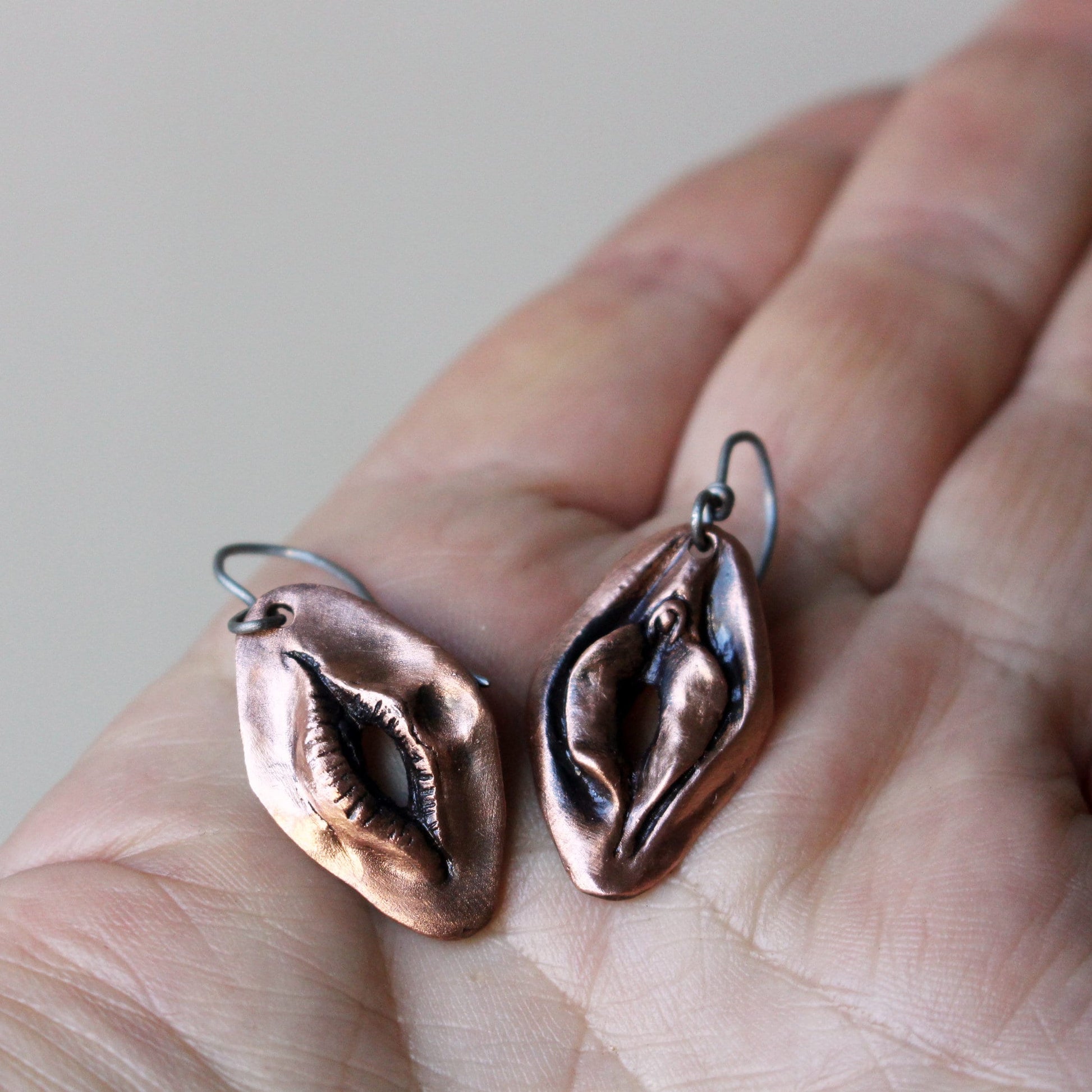 Reversible earrings, one side with a mouth and the other a vulva. Handcrafted in copper with titanium hooks
