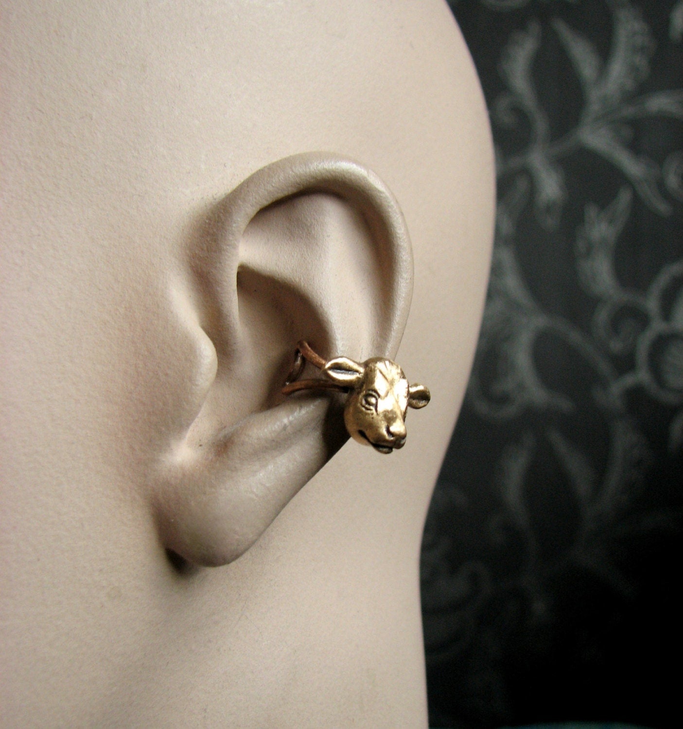 An ear cuff featuring a bronze cow head, displayed on a mannequin ear.