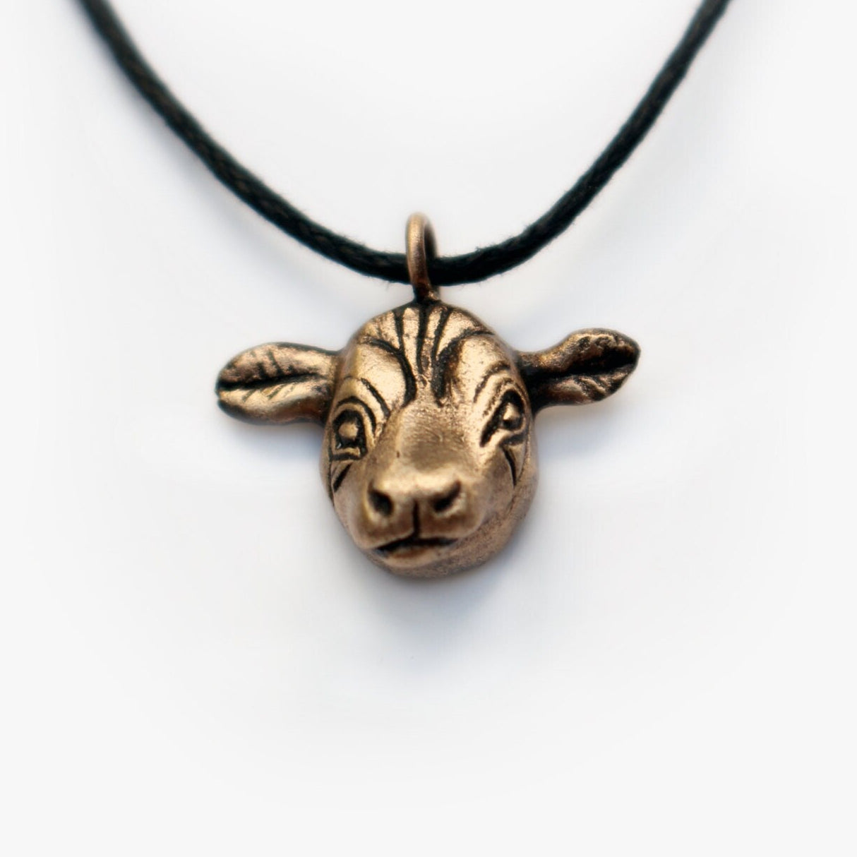 Bronze cow head pendant on a black cord against a white background
