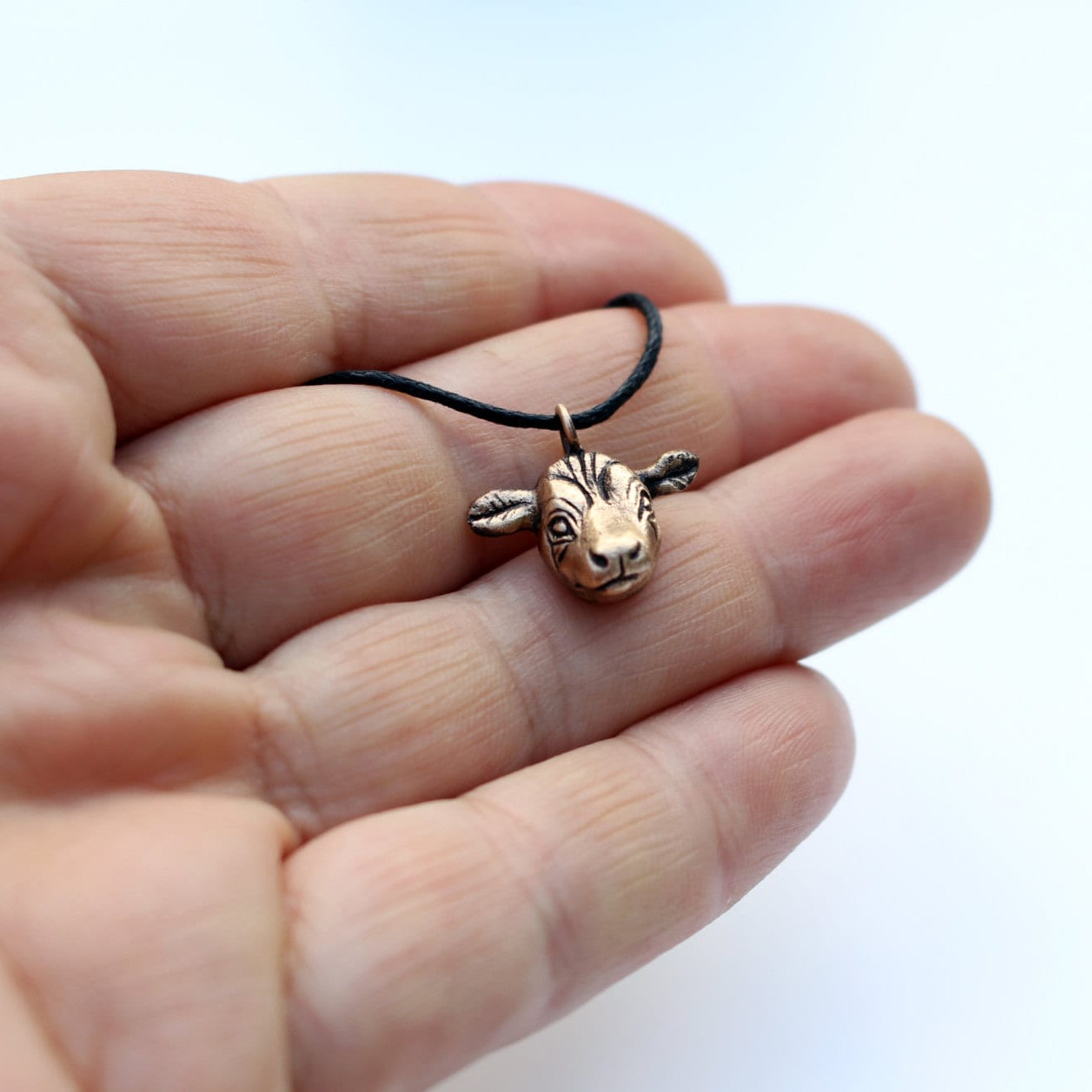 Bronze cow pendant on a black cord held in a hand