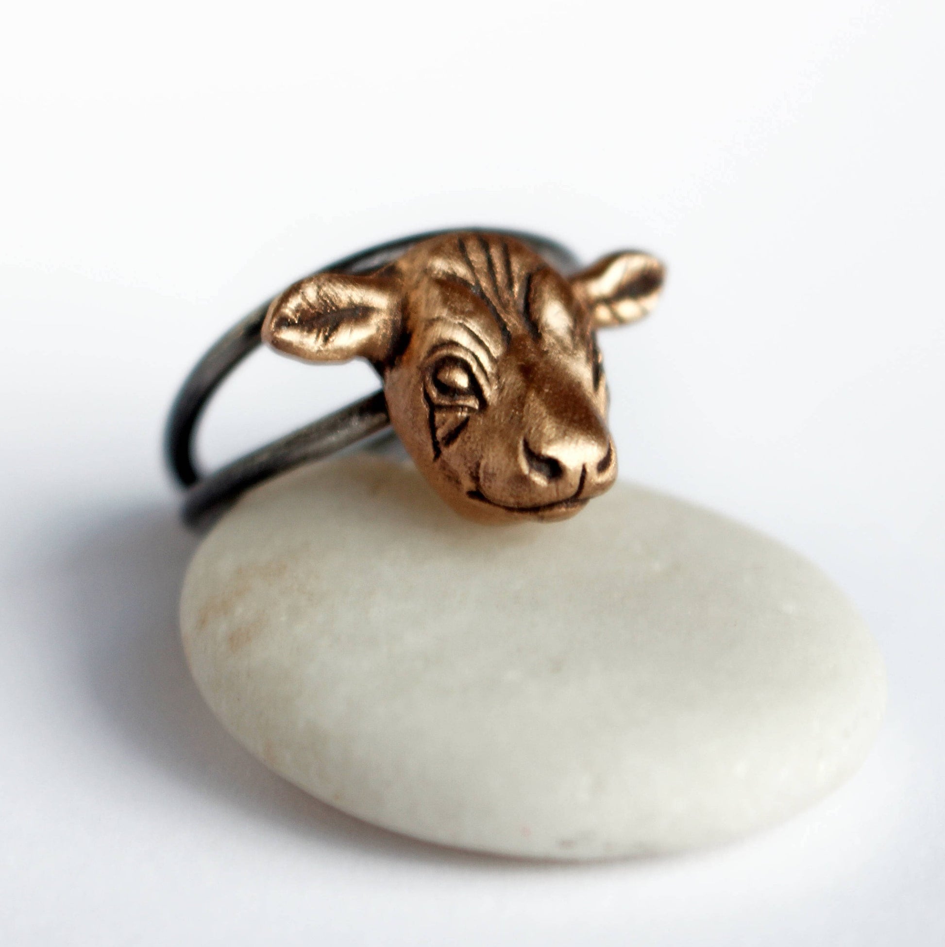 A bronze ring with a tiny cow head sculpted on top, placed on a white stone.