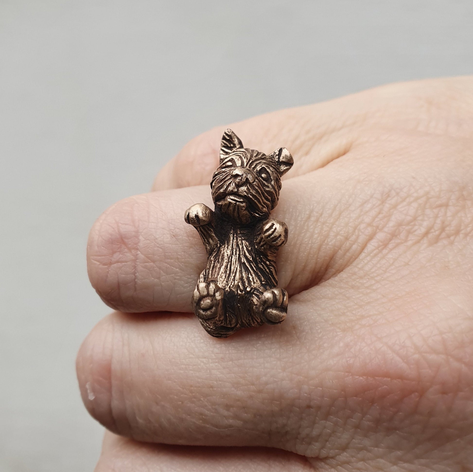 A handcrafted bronze ring featuring a small dog sculpture, displayed on a person's finger.