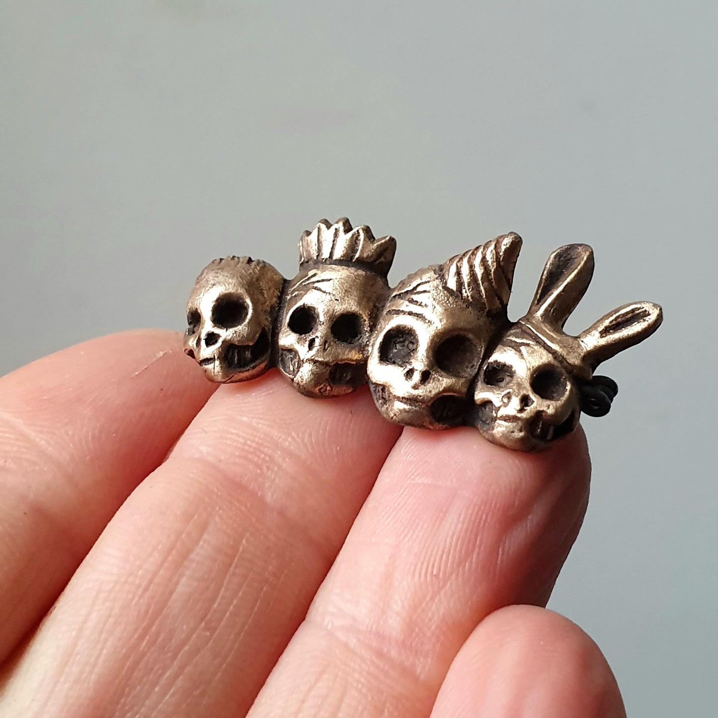 brosch med fyra döskallar i bartyhattar skulpterad i brons
