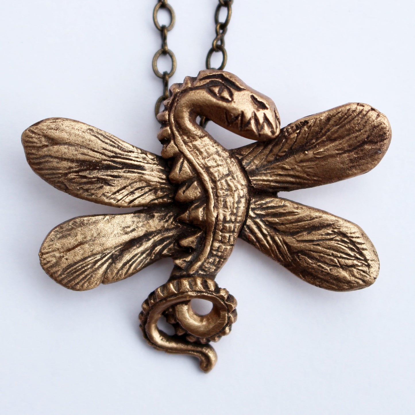A bronze necklace in the shape of a dragonfly dragon with detailed wings and body, displayed against a white background.