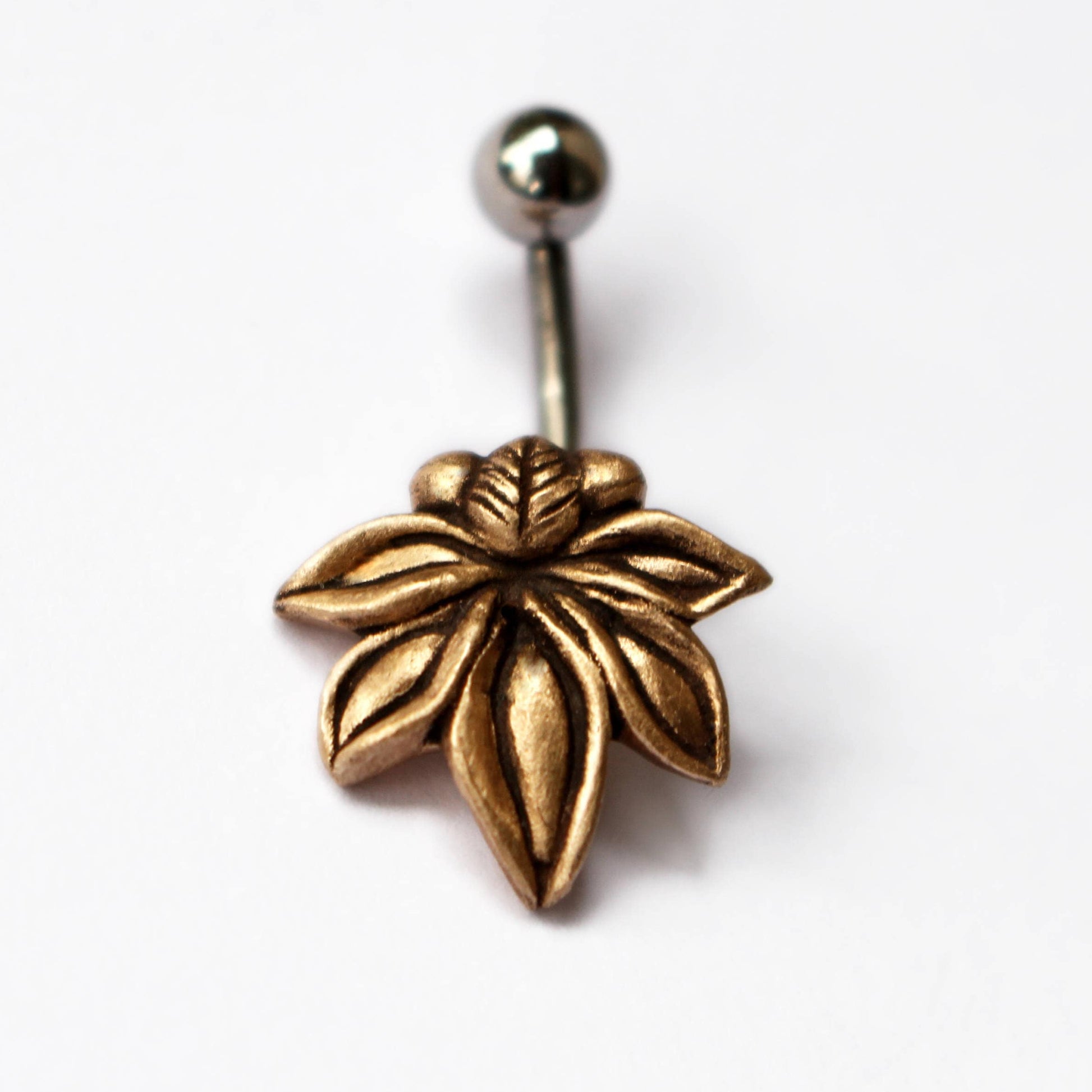 A bronze floral belly ring with a star anise seed pod shape attached to a curved barbell.