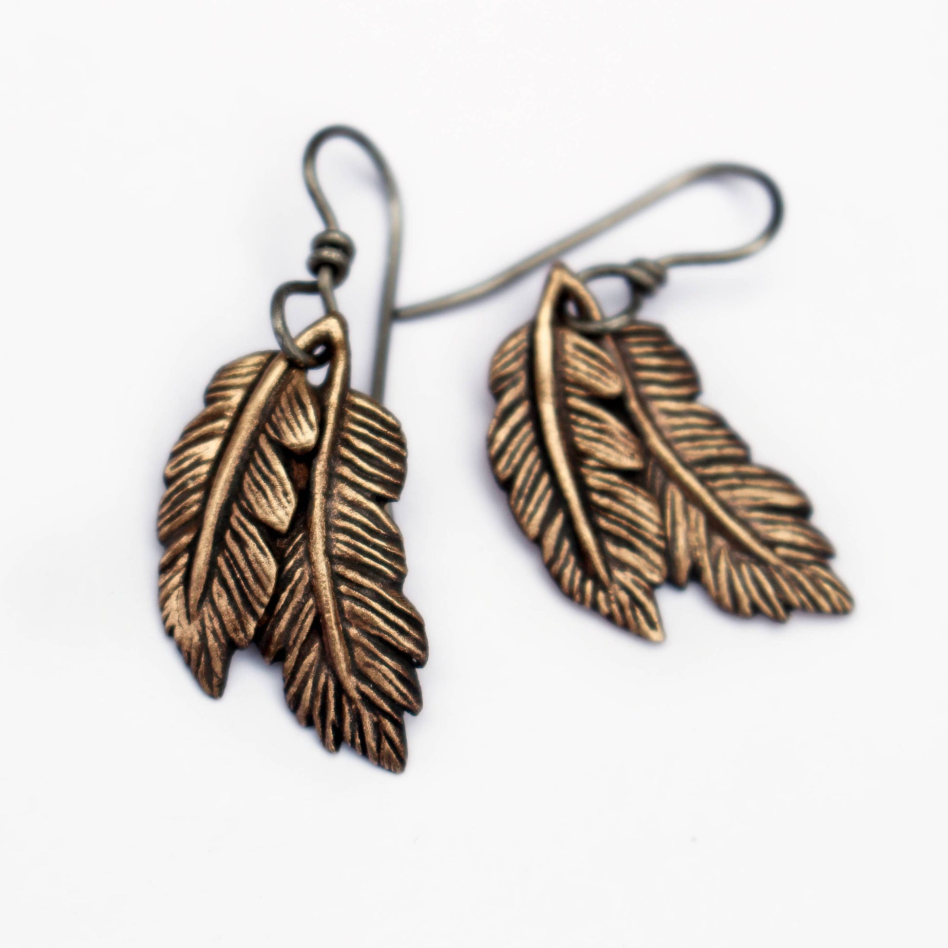 A pair of bronze and titanium dangling feather earrings with intricate detailing on the feathers.