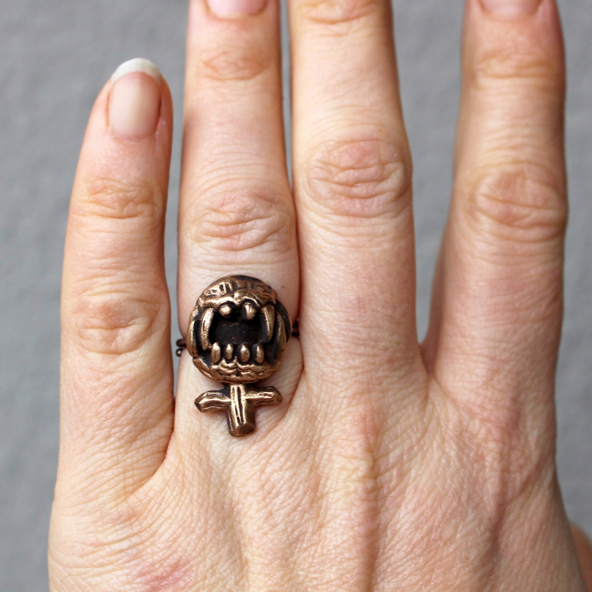 feministtecken skulpterad i brons med vassa tänder som fingerring
