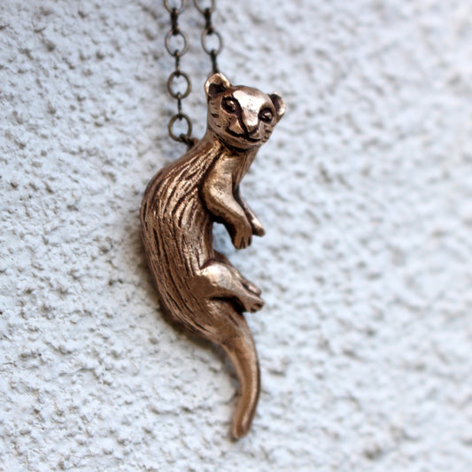 Bronze ferret polecat necklace pendant on a chain against a textured light background