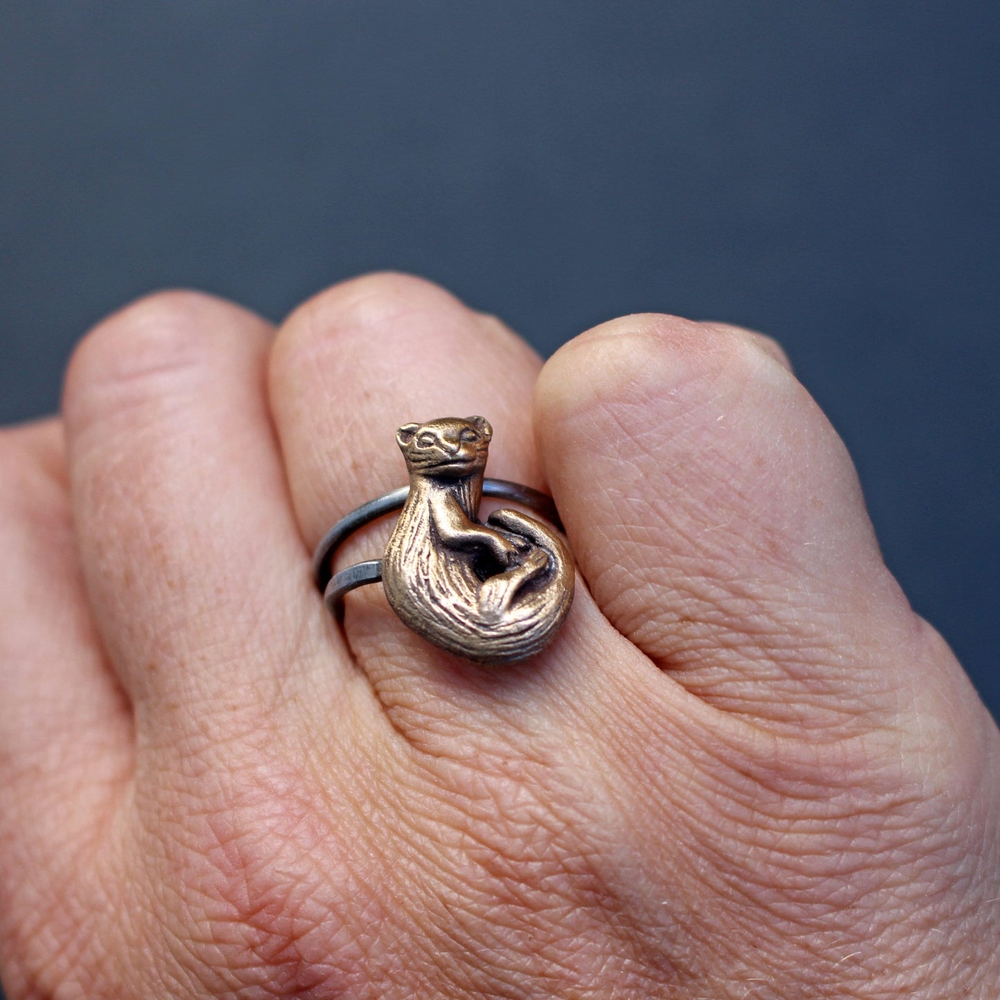 Hand wearing a ring made in bronze and stainless steel with a sculpted ferret polecat