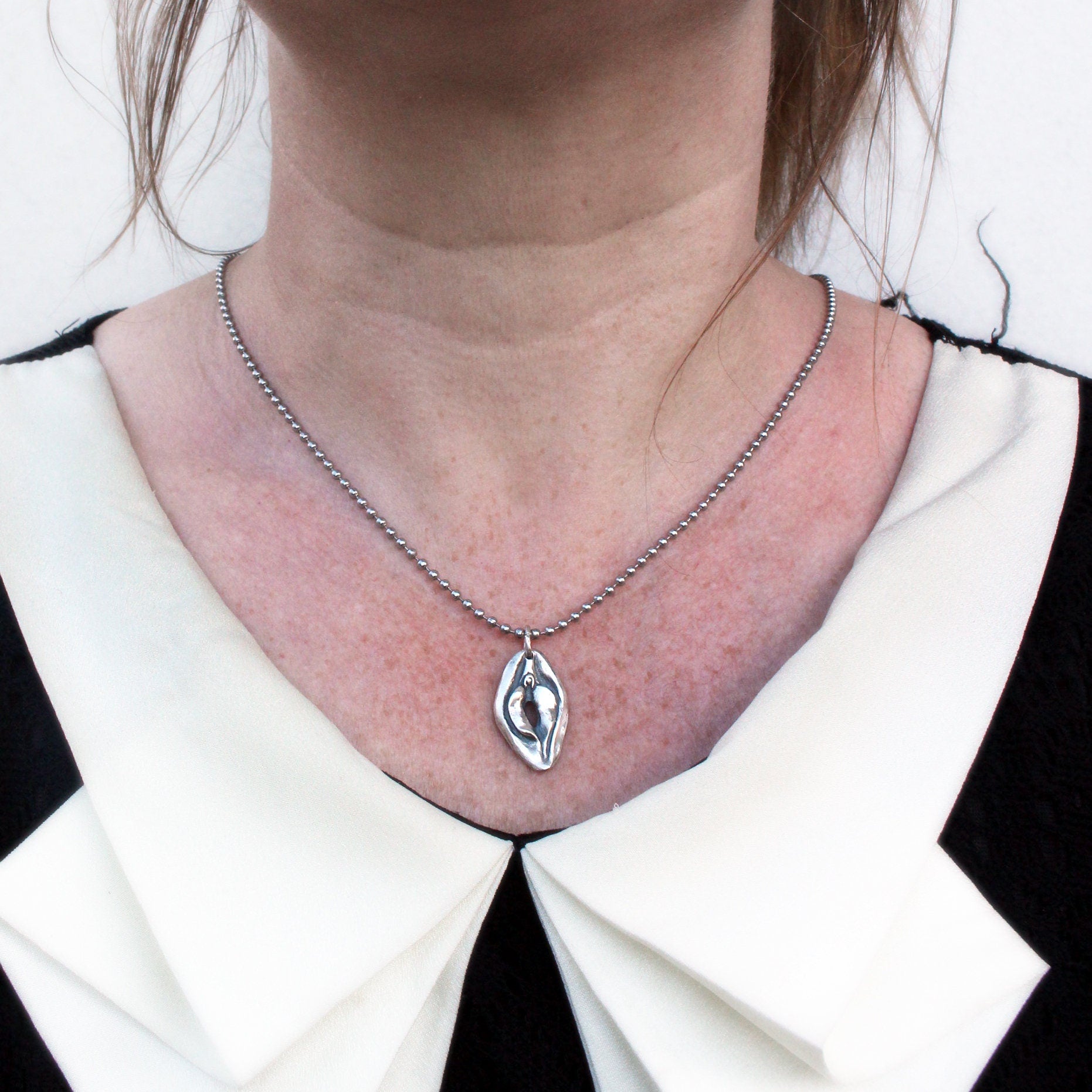 vändbart fitthalsband i sterling silver med en vulva på ena sidan och en mun på andra