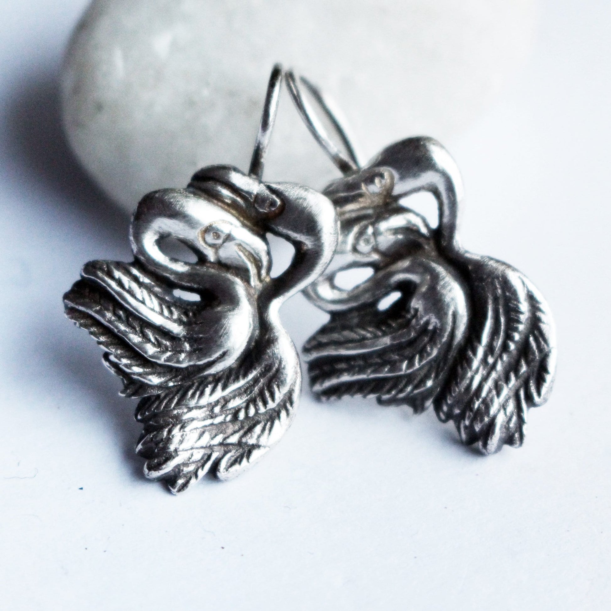 A pair of handmade flamingo earrings made of sterling silver or bronze, displayed against a light background.