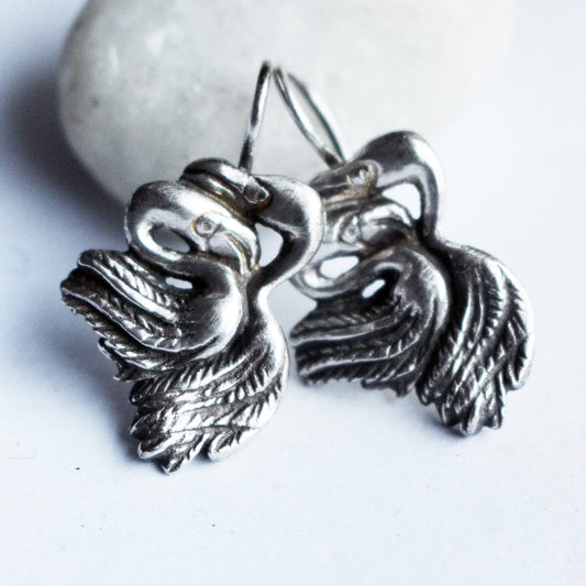 A pair of handmade flamingo earrings made of sterling silver or bronze, displayed against a light background.